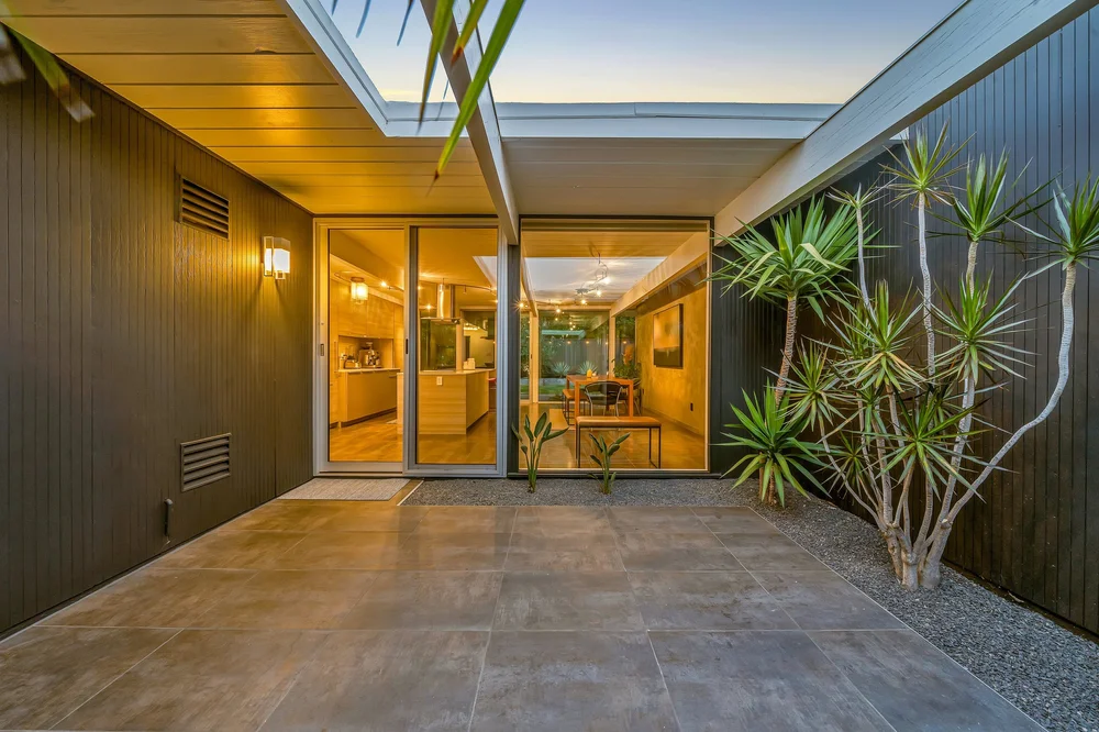 Open-air atrium at 1147 Pulora Court, with a tree, paving and glass walls looking into illuminated living rooms