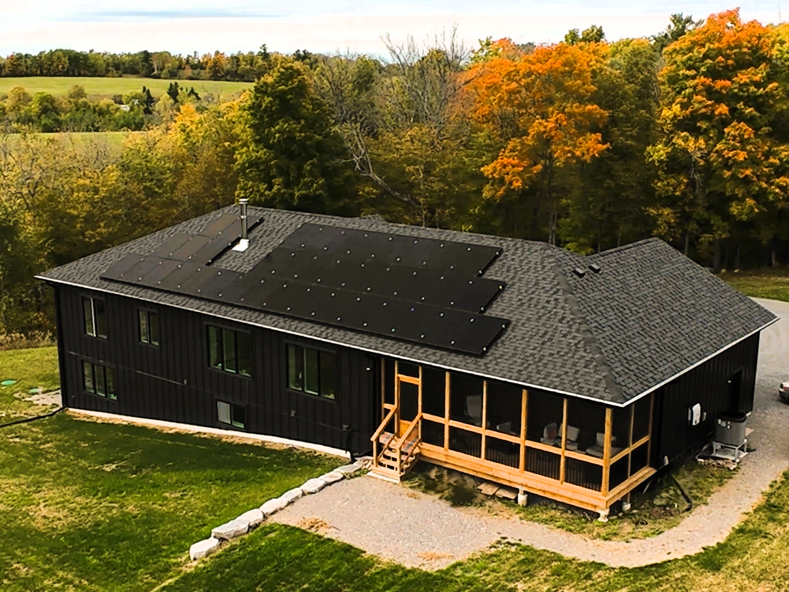 A black house with solar panels on the roof, surrounded by trees with fall foliage, and a small wooden deck at the entrance.