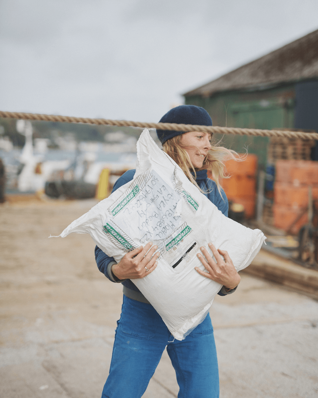 Woman in a blue beret carrying a sack of panela cane sugar across a harbour quay (Copy)