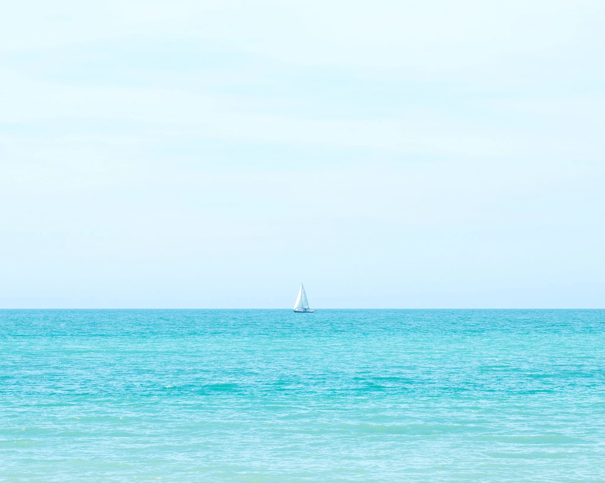 Lone sailboat on tranquil turquoise sea under clear sky
