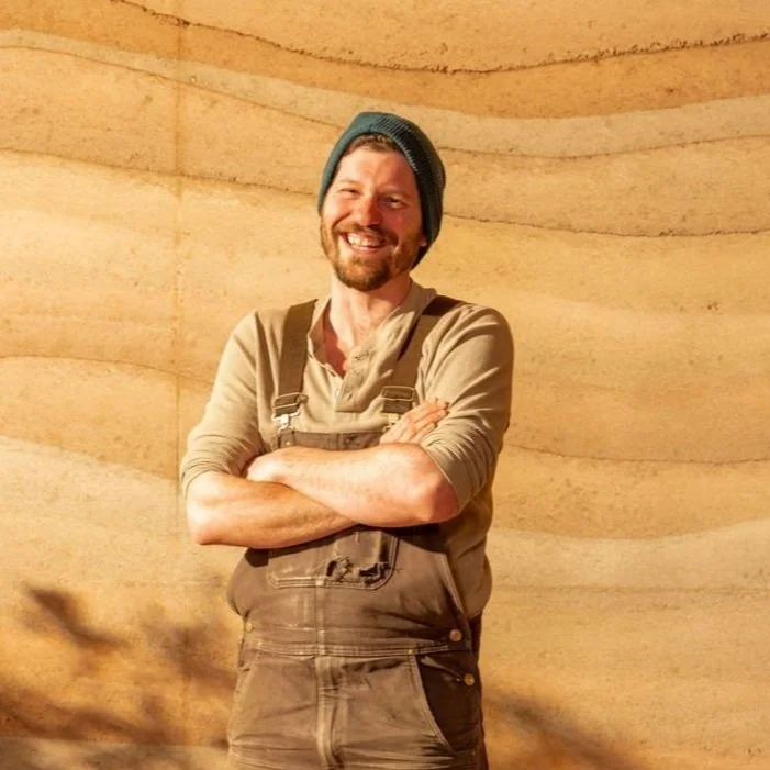 Graham Cavalier, general manager of Aerecura Sustainable Builders, smiling at the camera in front of rammed earth.