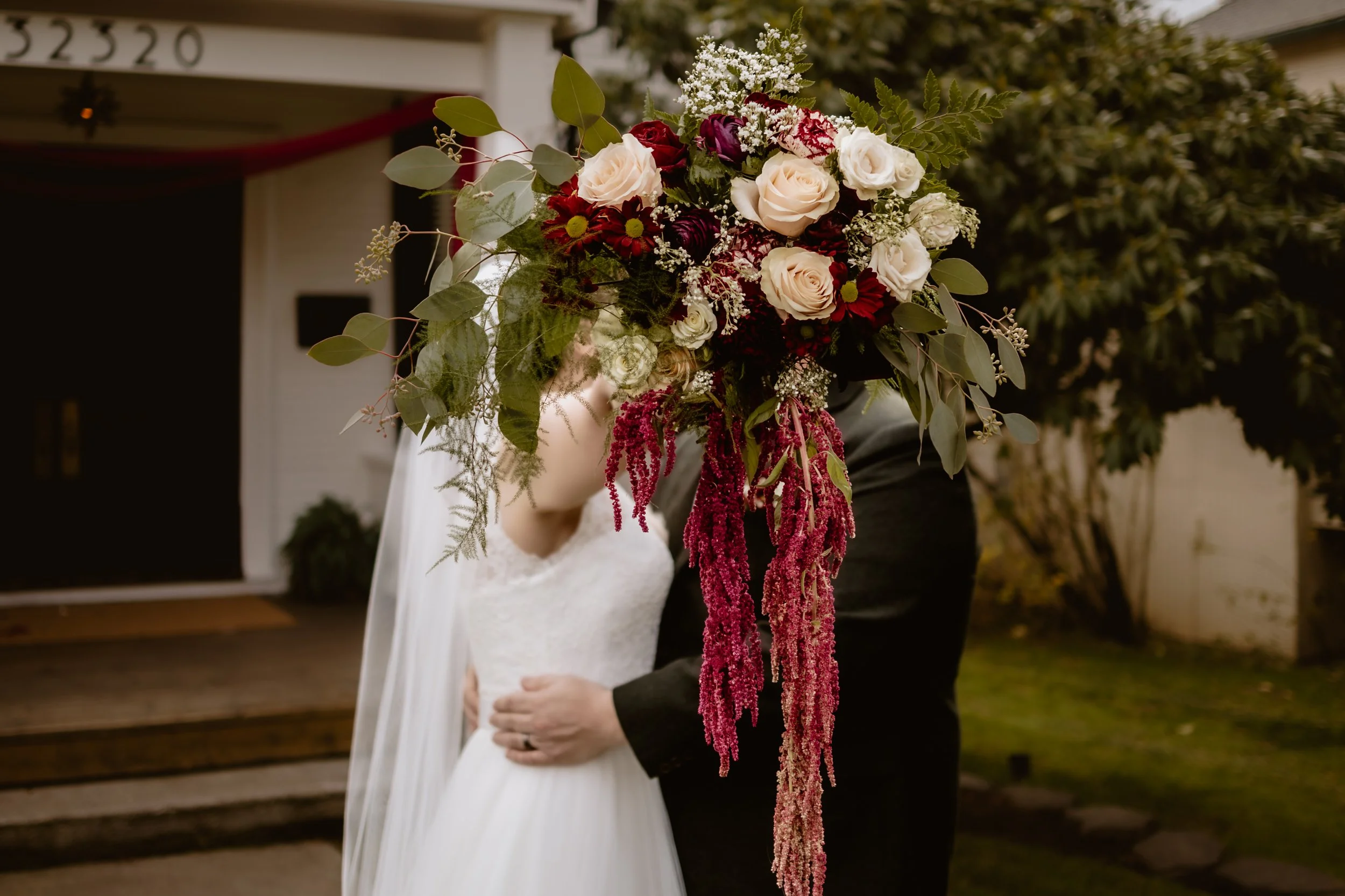 Bride and groom behind a dramatic burgundy and white fall wedding bouquet