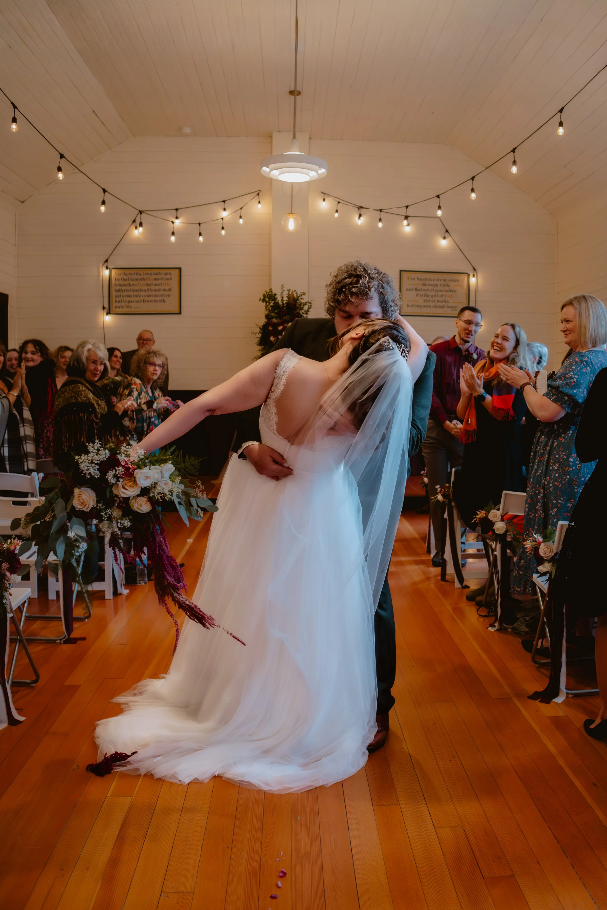 Wedding couple share a kiss in the aisle at Hummingbird Hall