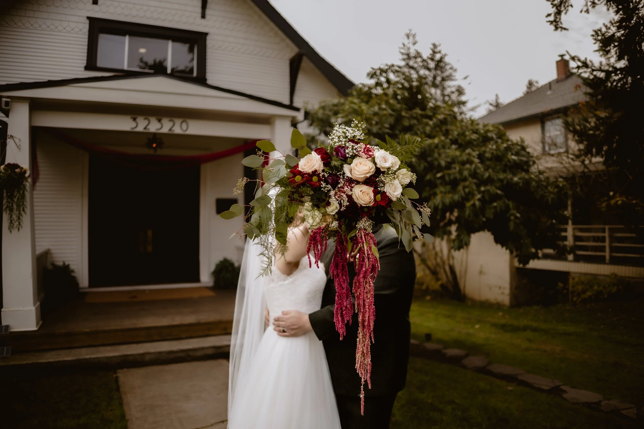 Bride and groom behind a dramatic fall bouquet outside Hummingbird Hall