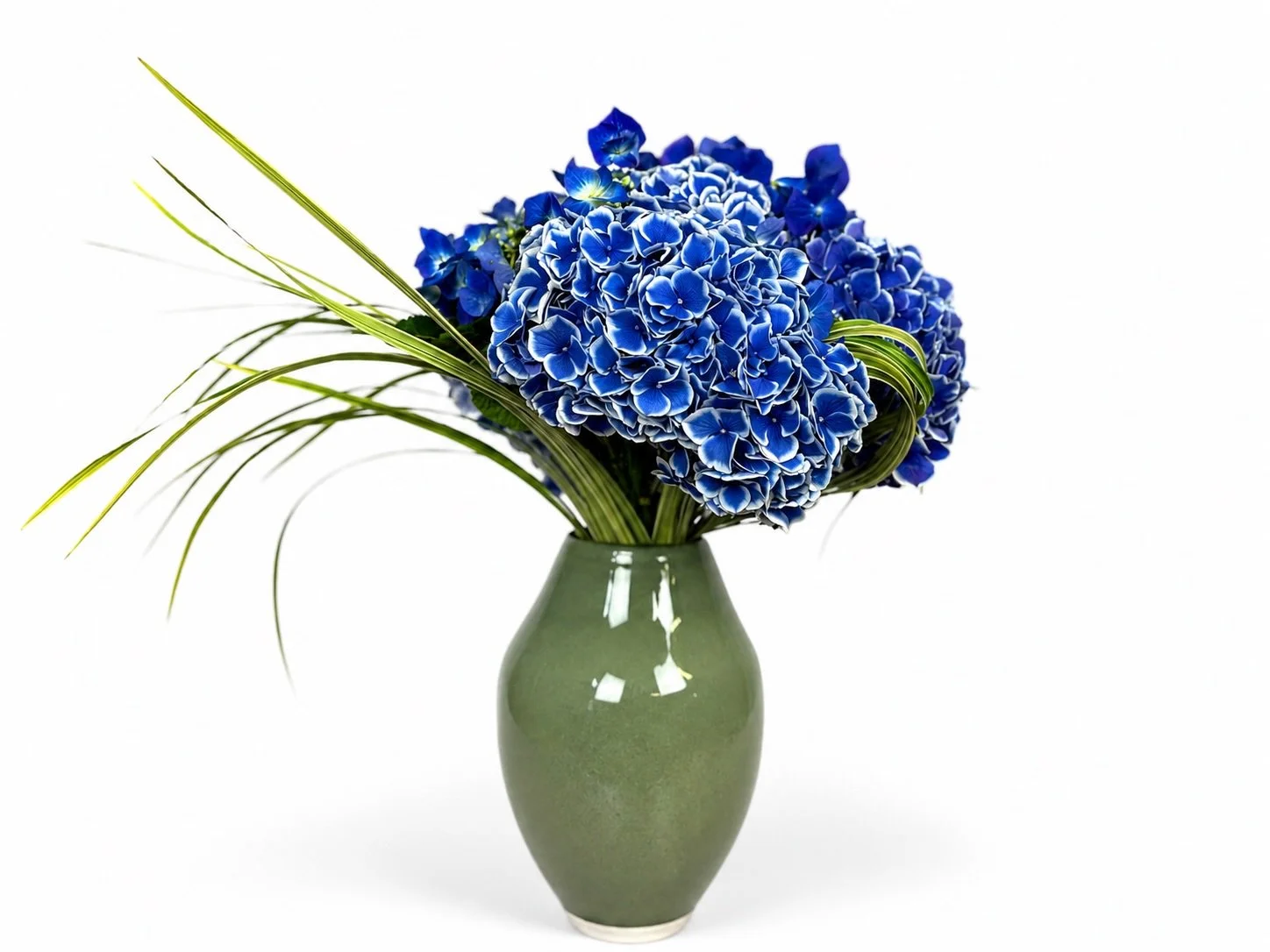 Sea Spray &mdash; our June arrangement.

A cool, coastal composition of vivid blue hydrangea, delicate blue accent blooms, and sweeping lily grass, arranged in a softly rounded green ceramic vase.

Fresh, sculptural, and quietly dramatic, Sea Spray b