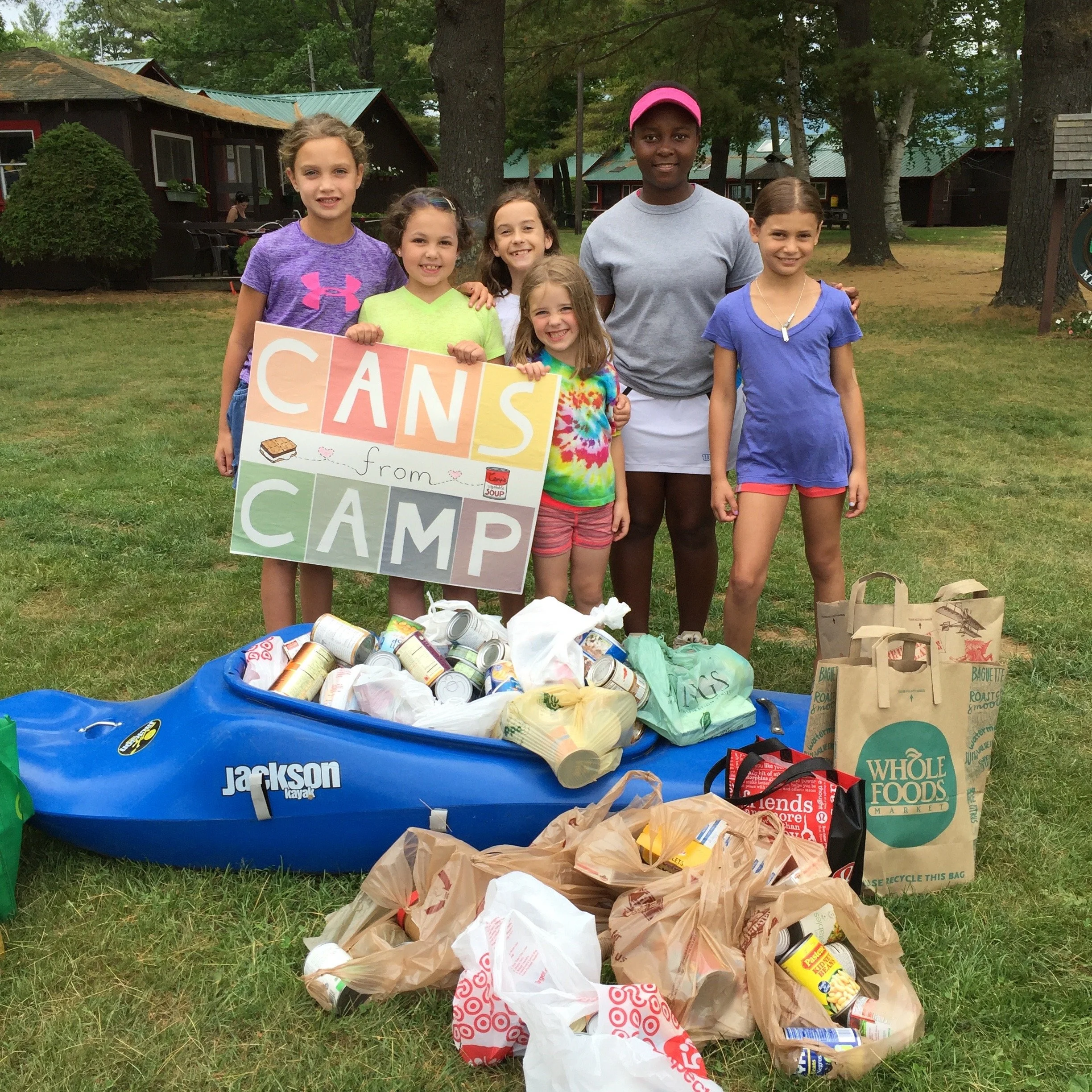 A successful morning for Camp Merriwood's Cans From Campers food drive. Image shows 5 happy girls behind a bright blue kayak full of donations