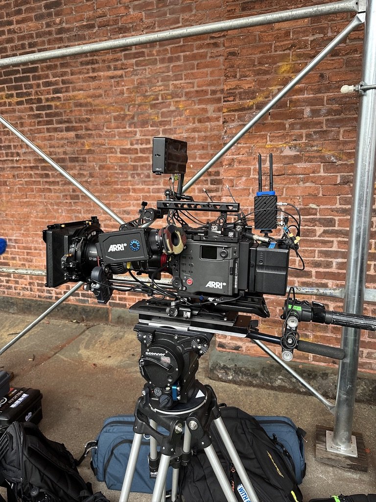 Professional film camera setup on tripod with accessories in front of a brick wall.