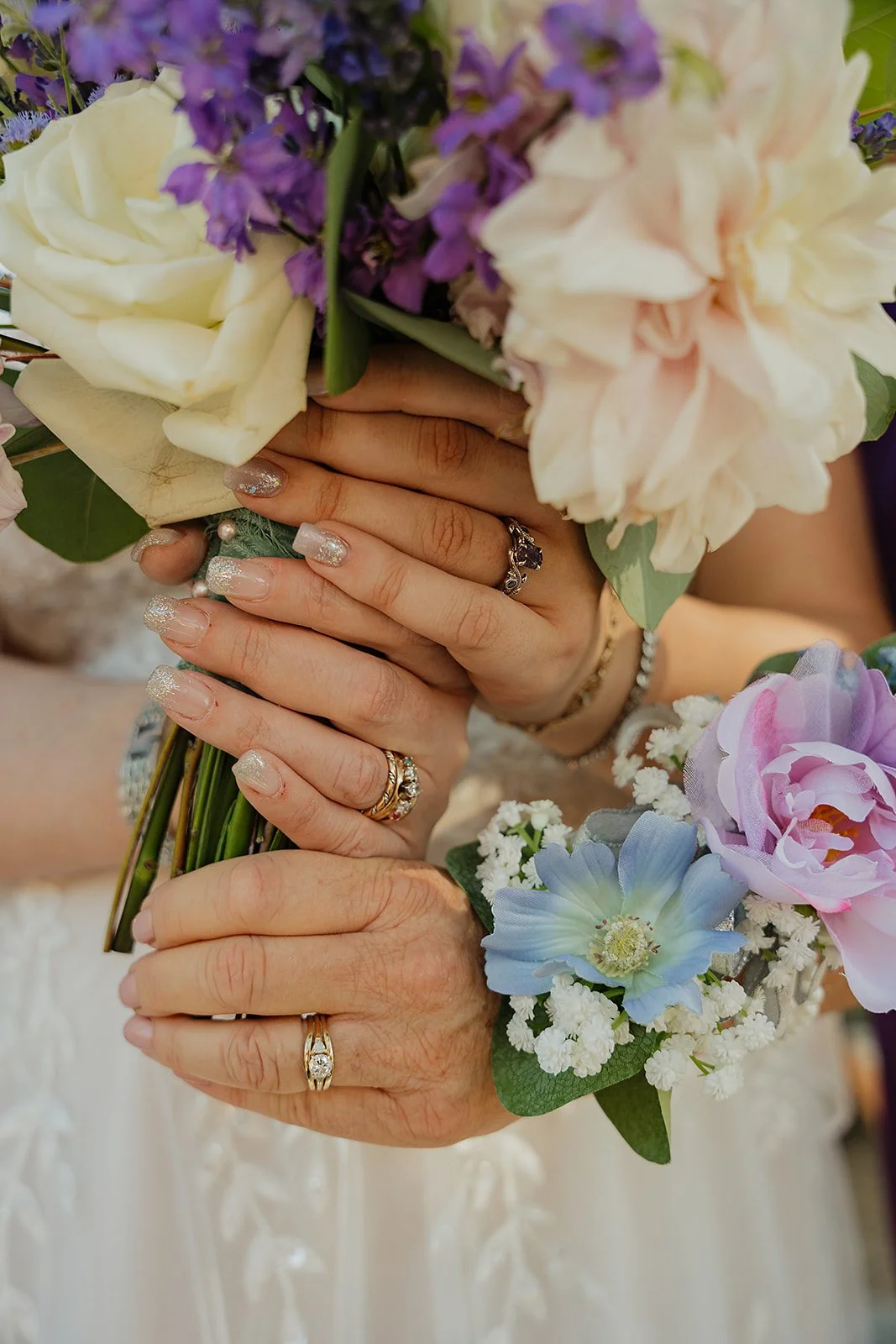 Close-up of two hands holding a bouquet of flowers, both wearing rings on their ring fingers.
