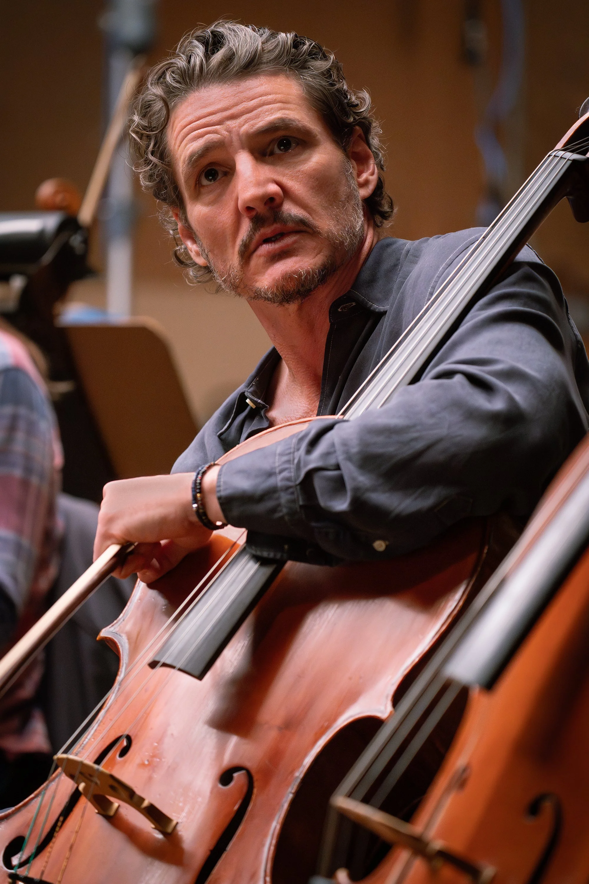 Pedro Pascal, bow in hand, looks off-camera while leaning on a large string instrument in a still from Behemoth.