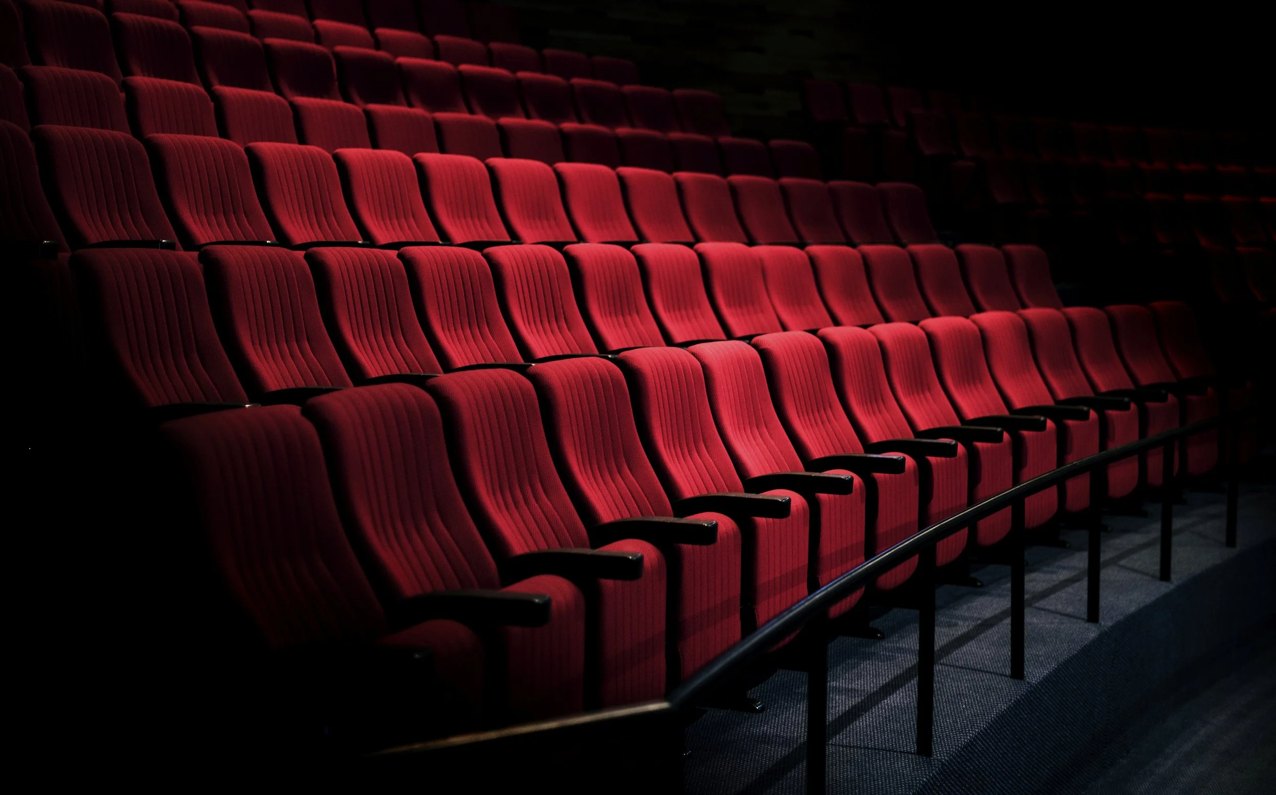 Empty red theater seats with armrests, in a darkened auditorium.