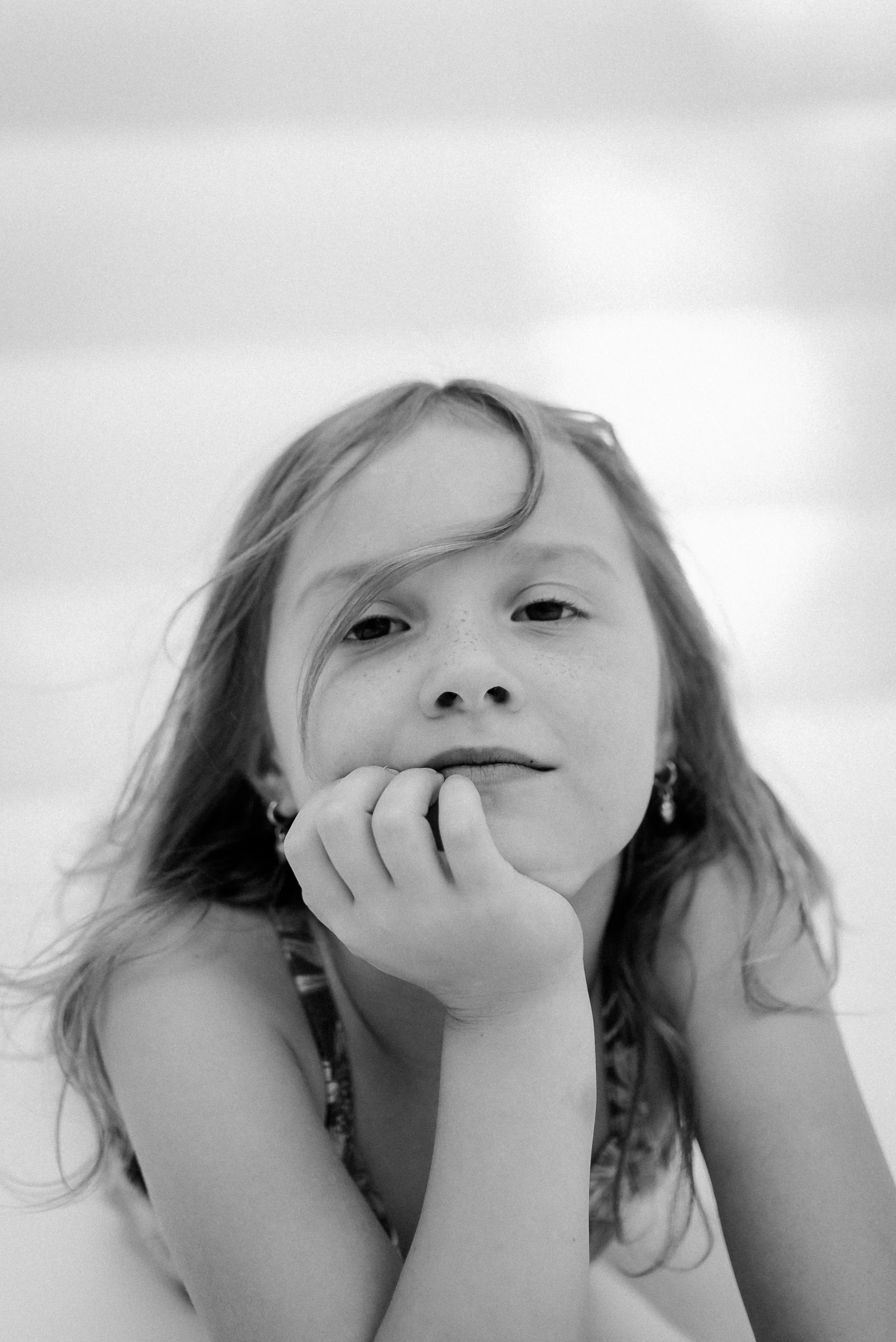 A black and white portrait of a young girl with long hair, resting her chin on her hand and looking at the camera.