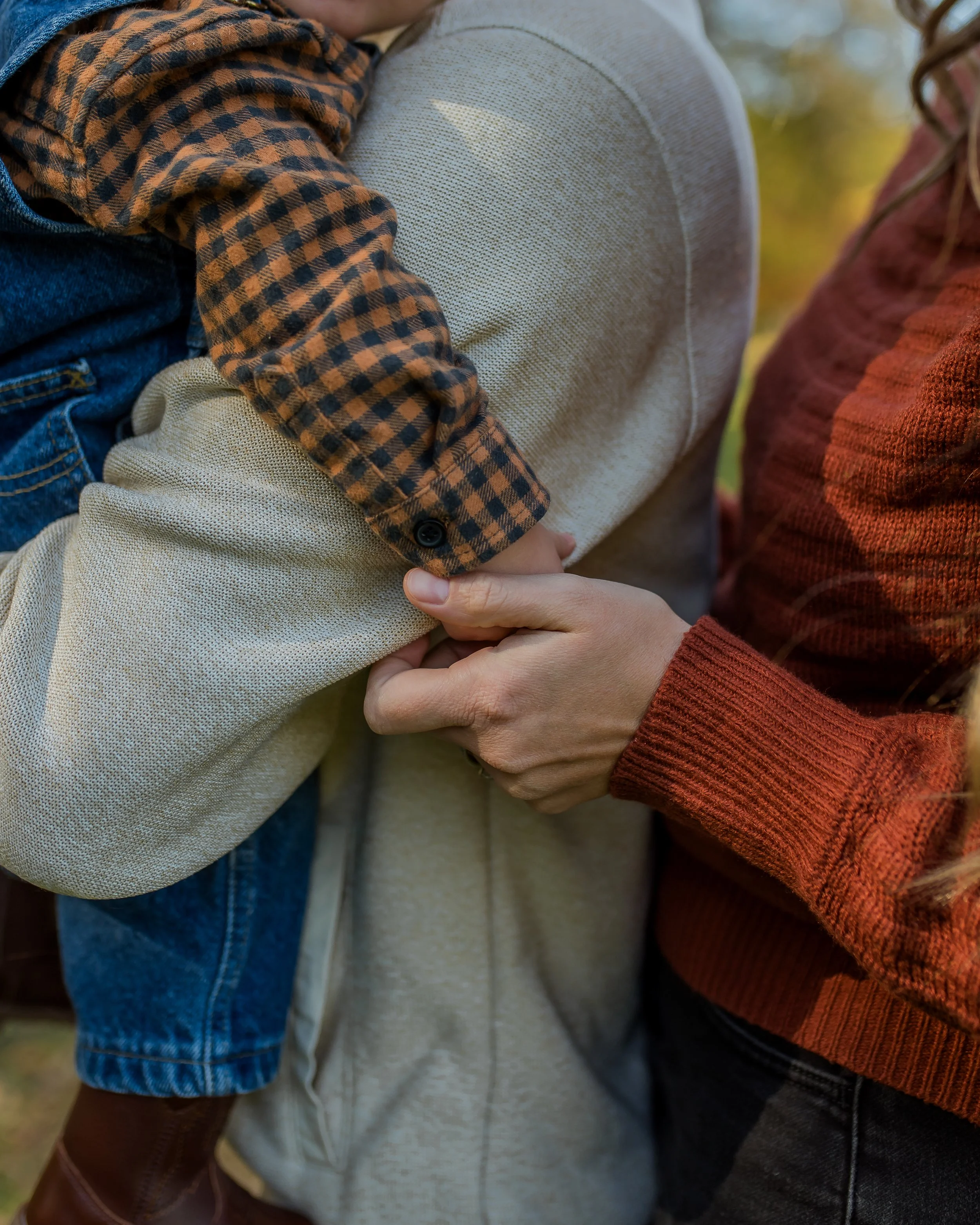 A woman holding a child by the arm outdoors with trees in the background.