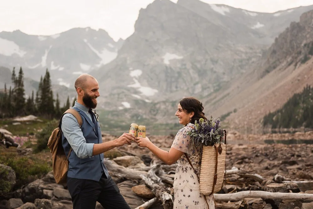 A couple toast beers after their elopement on the shores of an alpine lake near Boulder, Colorado