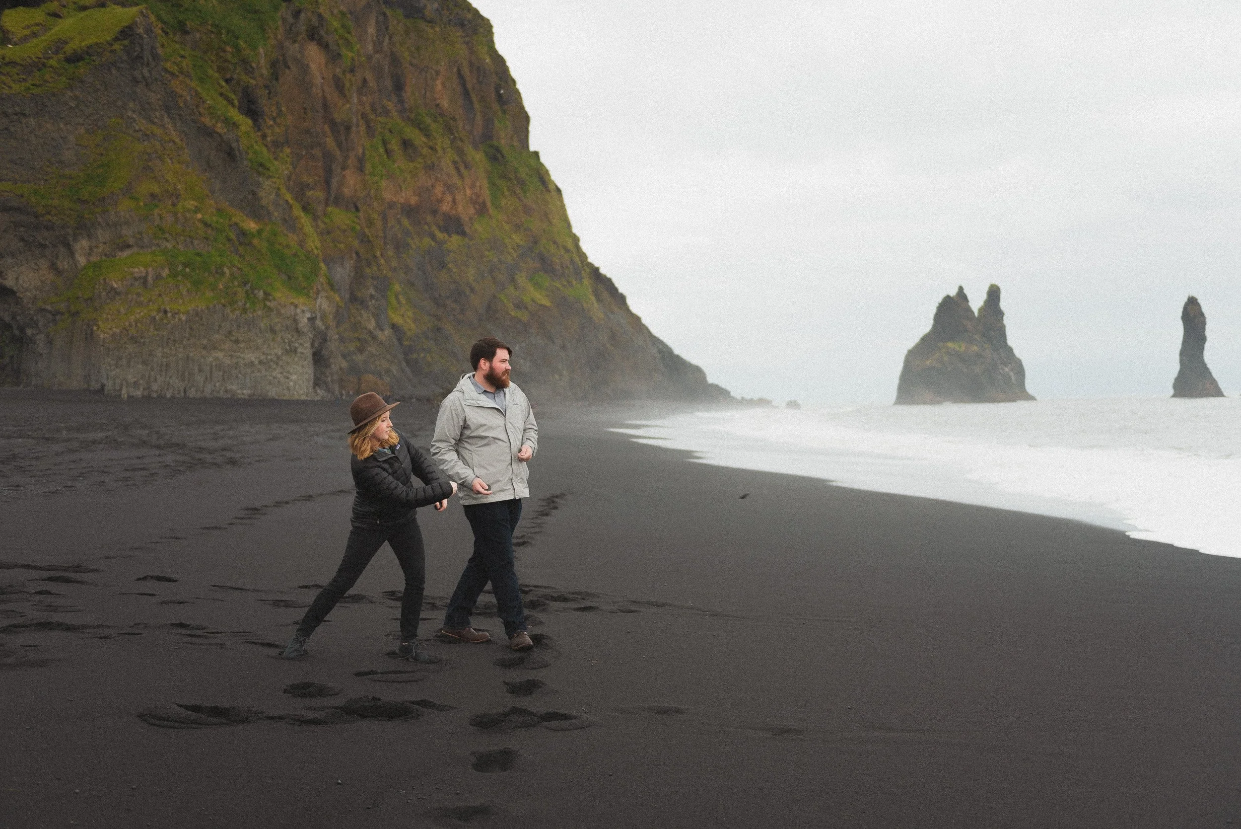 A couple in casual clothes skip stones on their honeymoon at the black sand beach in iceland