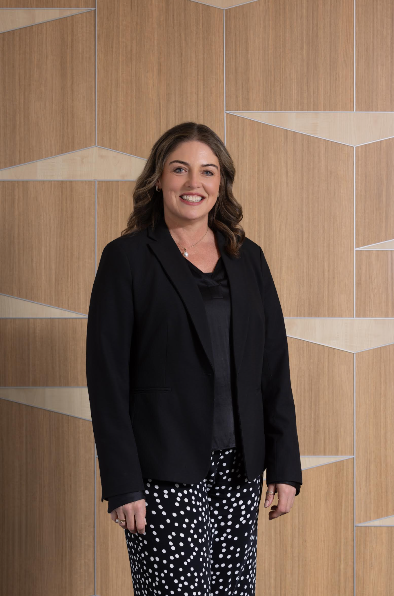 Smiling woman with crossed arms, standing in front of a geometric wooden wall.