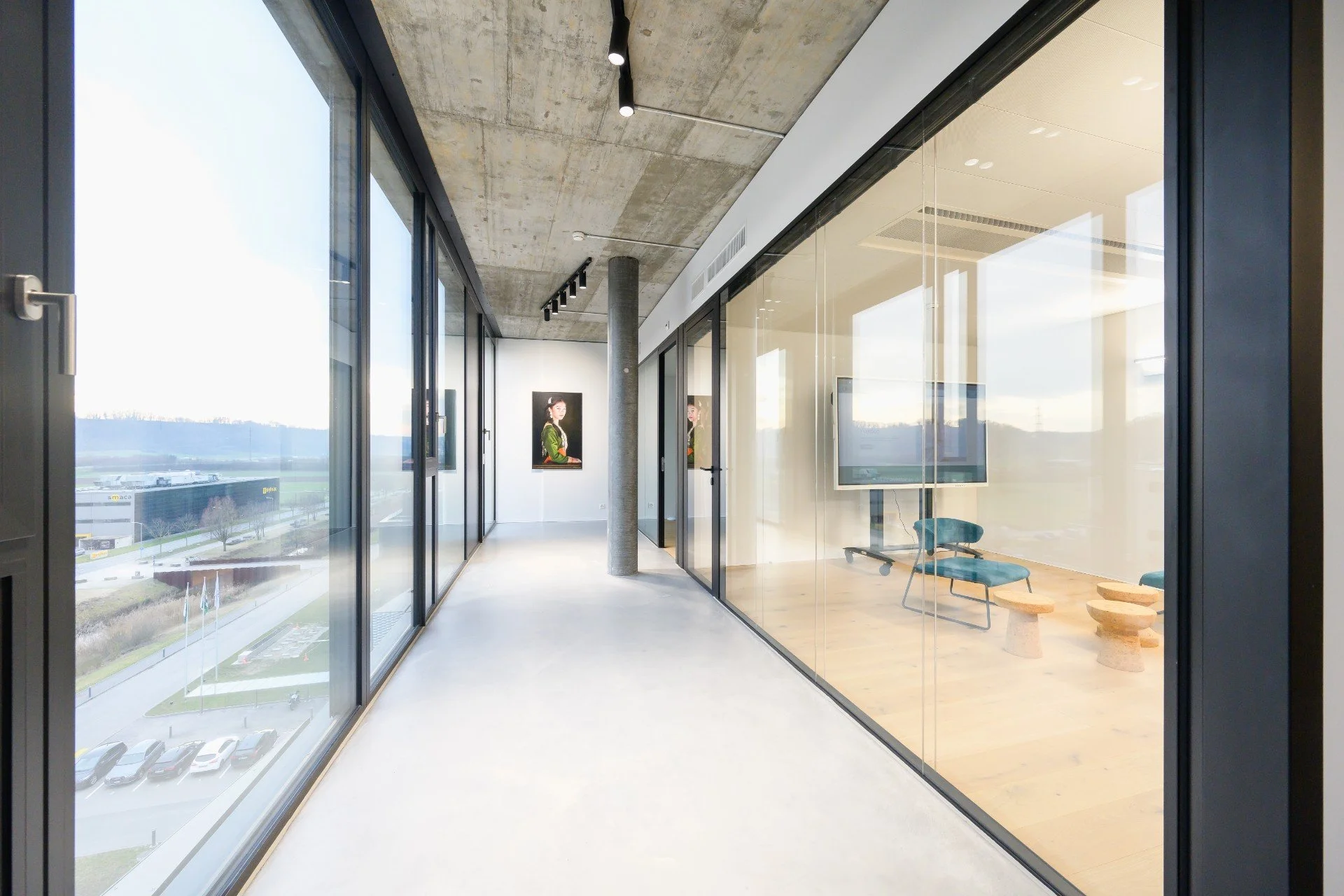 Couloir avec baie vitrée donnant sur l'extérieur à gauche, et baie vitrée donnant sur une salle à droite. 