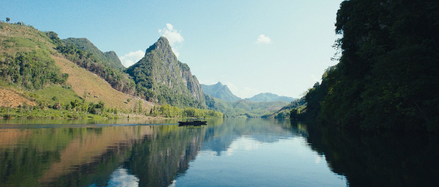 Une vue d'une rivière calme entourée de montagnes verdoyantes sous un ciel clair et ensoleillé.