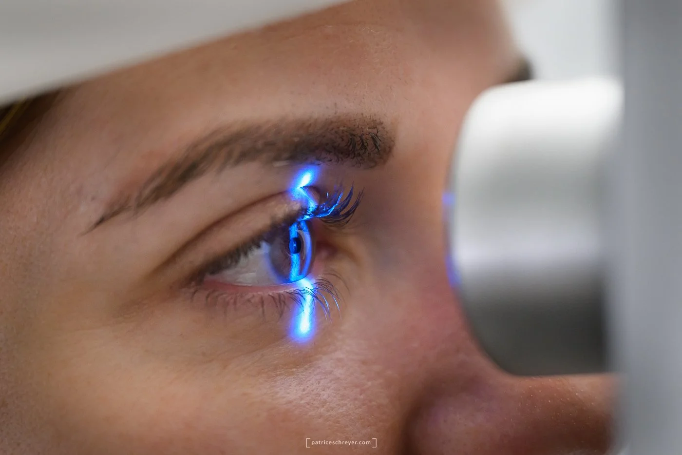Une femme subit un examen de l'œil avec un appareil utilisant une lumière bleue, tandis que le technicien regarde à travers une lentille pour évaluer la santé de l'œil.