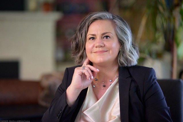 Professional headshot of Amy Morales, M.Ed.;HWC with short gray hair wearing a blazer and blouse, seated in a softly lit office setting.