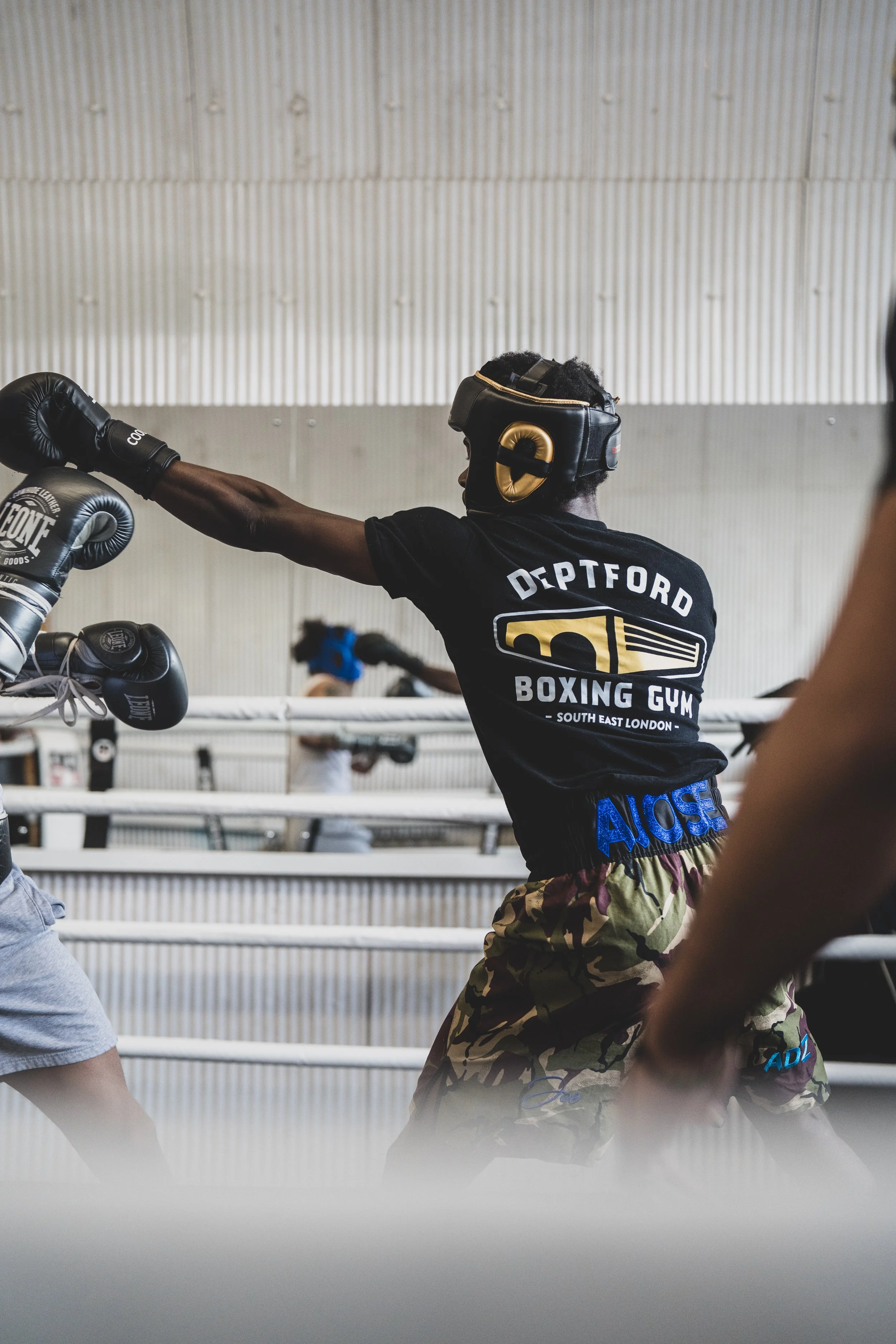 A young male boxer wearing protective headgear and boxing gloves practicing punches in a boxing gym.