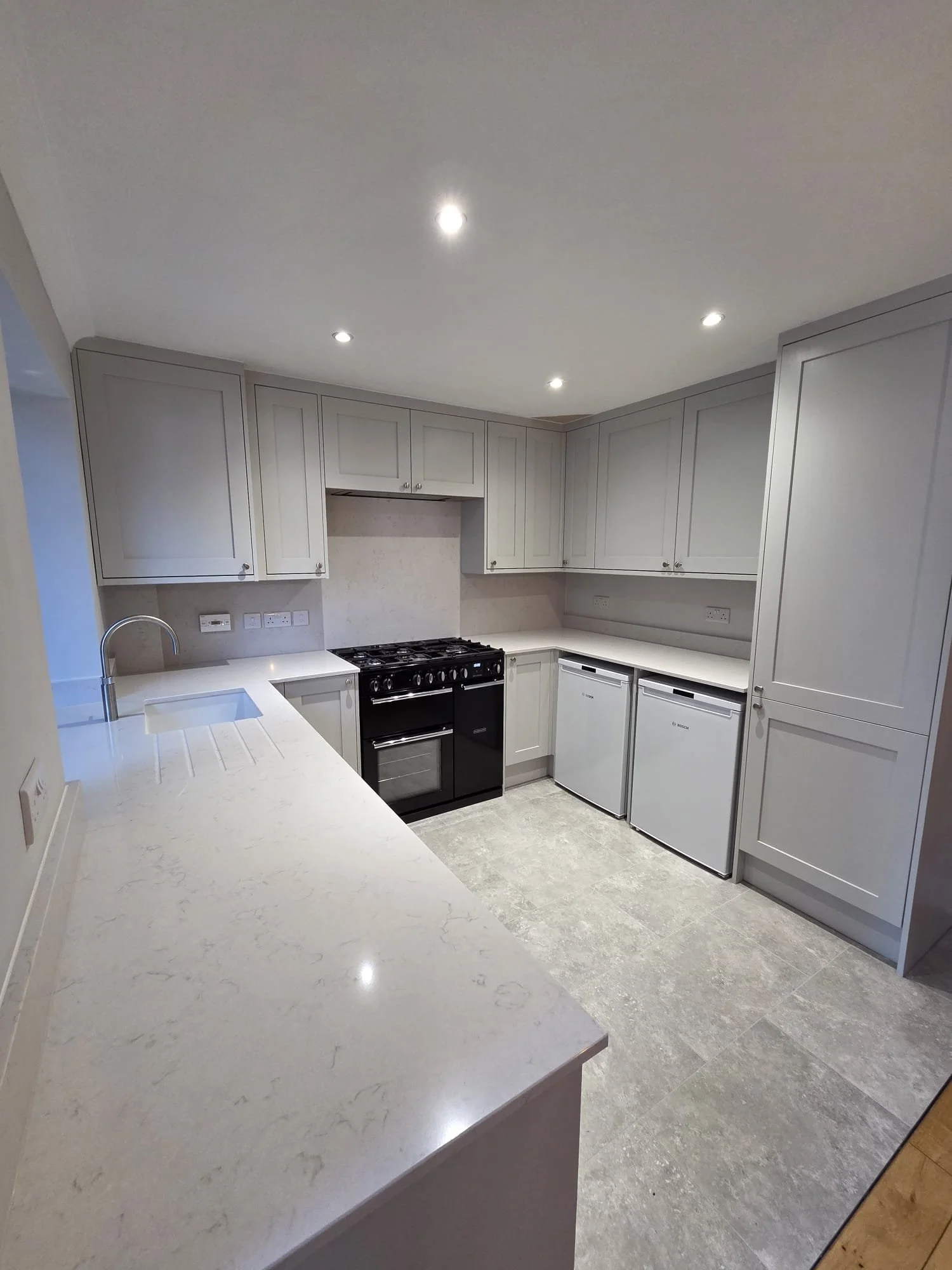 Modern kitchen with navy blue cabinets, white marble countertop, and a white oven. The oven has a digital display and two control knobs, with a label indicating a 2-year warranty. There's a marble backsplash and a window on the left side.