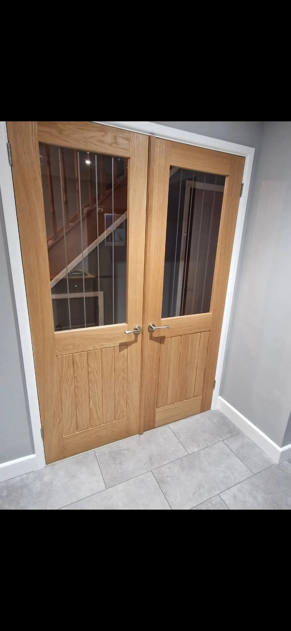 Wooden double doors with glass panels and metal handles leading to a staircase.