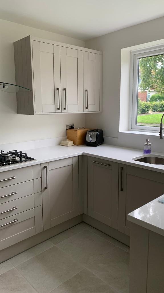 Modern L-shaped kitchen with white cabinets, gray drawers, a window overlooking a yard with green grass and trees, and a countertop with a coffee maker, a wooden box, and a soap dispenser.