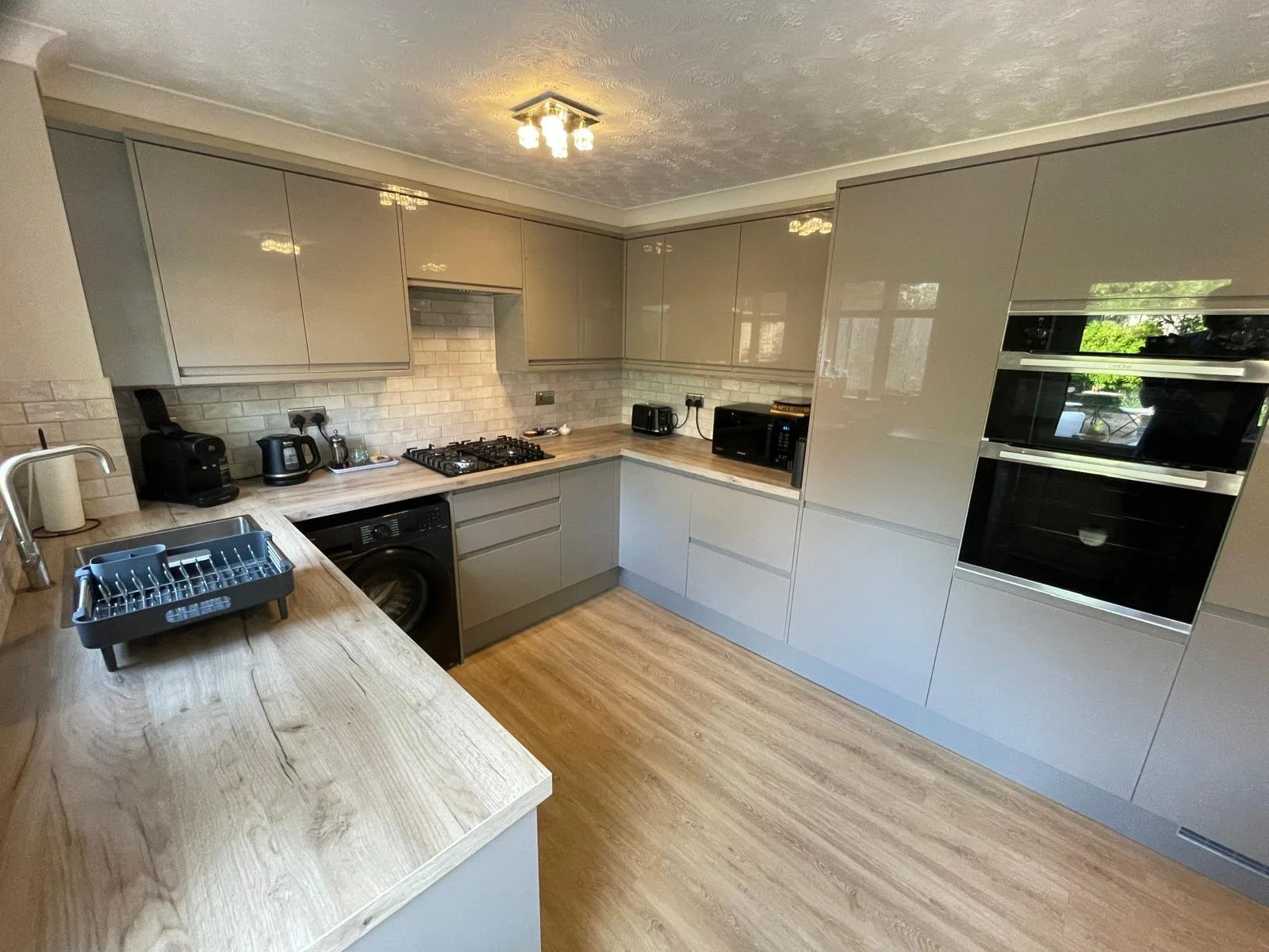 Kitchen completed with new gray cabinets, beige countertops, and black appliances, with finished floor and tiling.