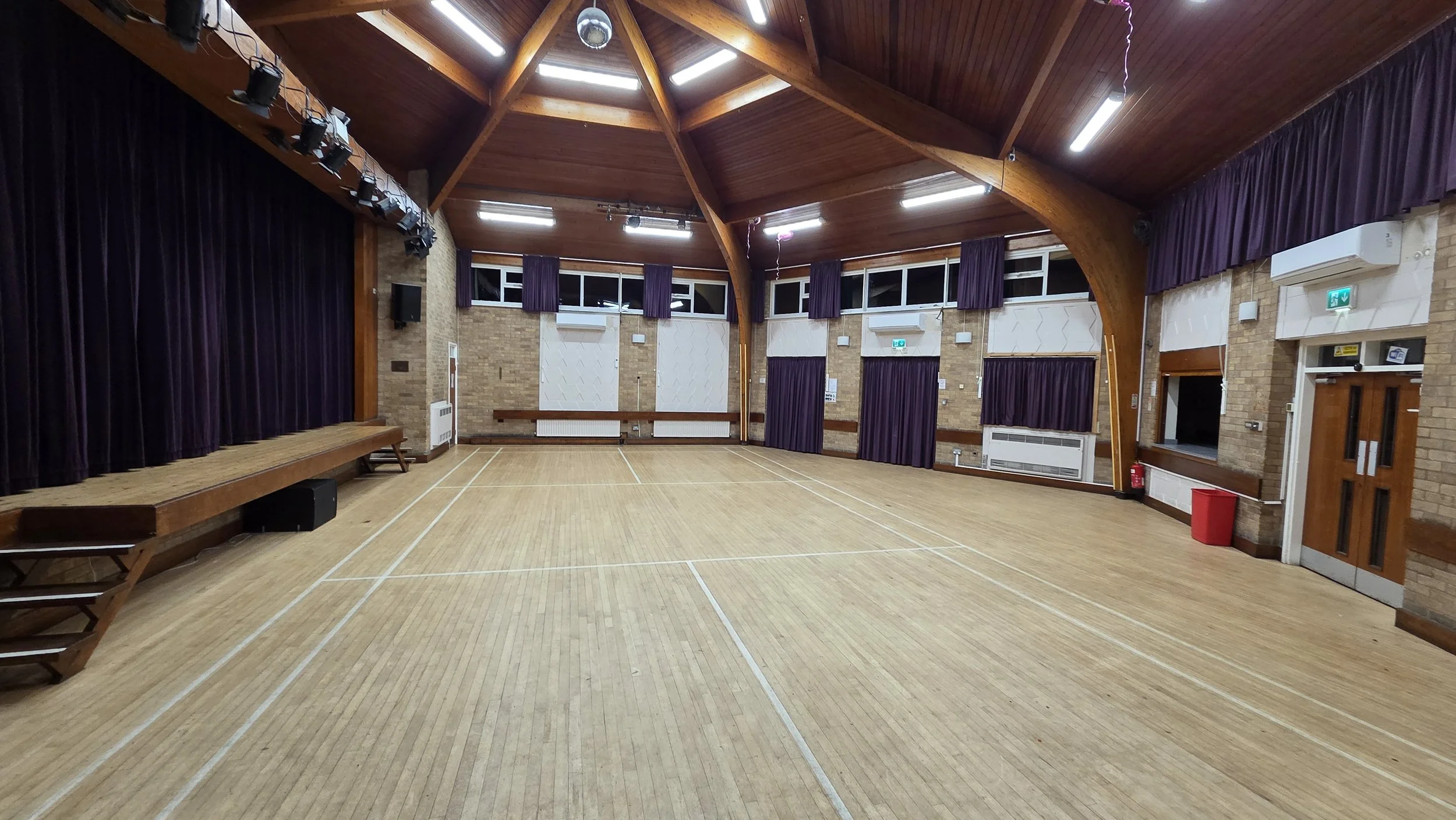 This is the main hall taken from the Brammer Room entrance. On the left is the stage and on the right is the kitchen servery hatch and main antrance doors. Slightly right of centre is the chair store and double fire exit doors.