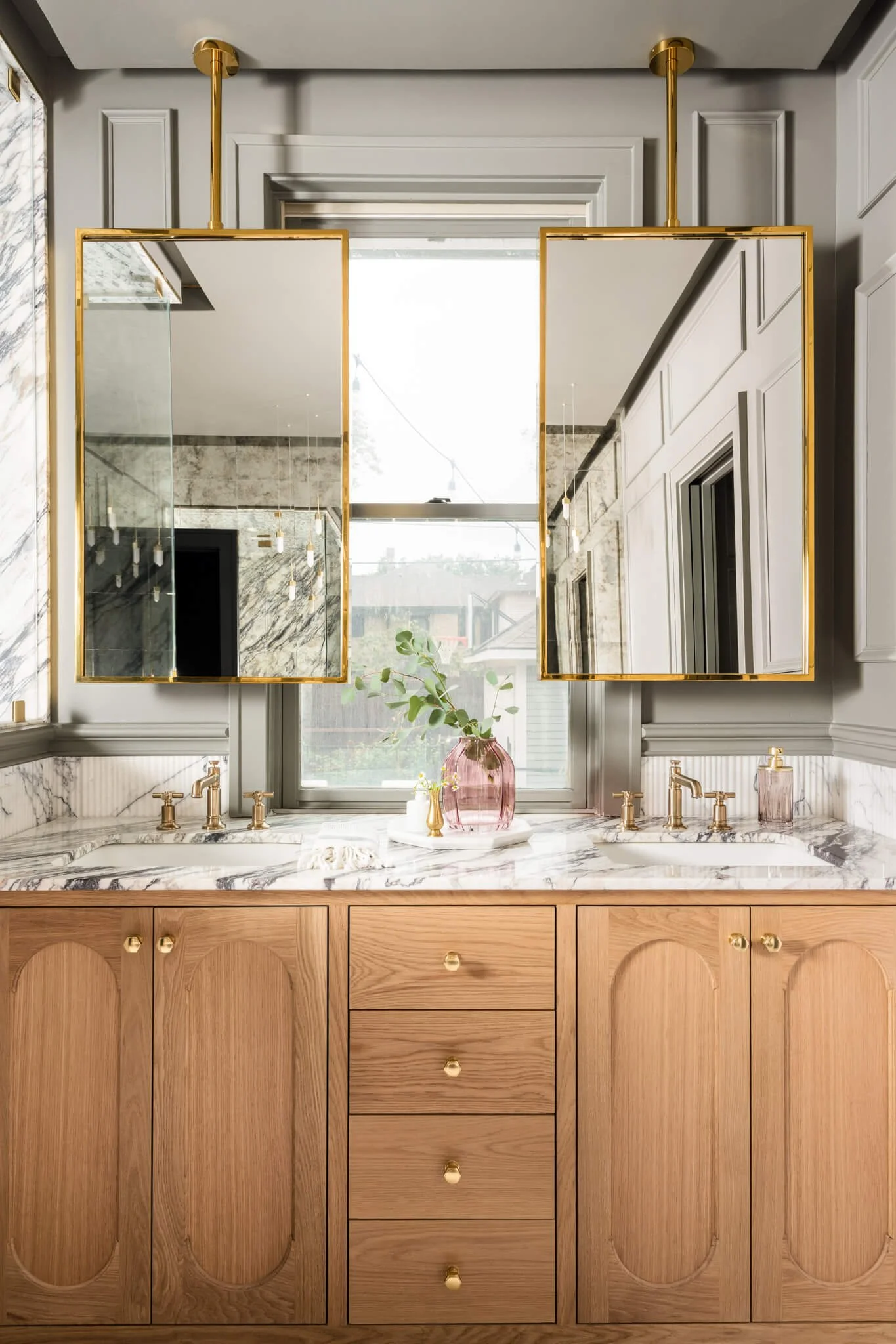 Double vanity bathroom with warm wood cabinetry, marble countertops, and oversized gold framed mirrors in a luxury home.