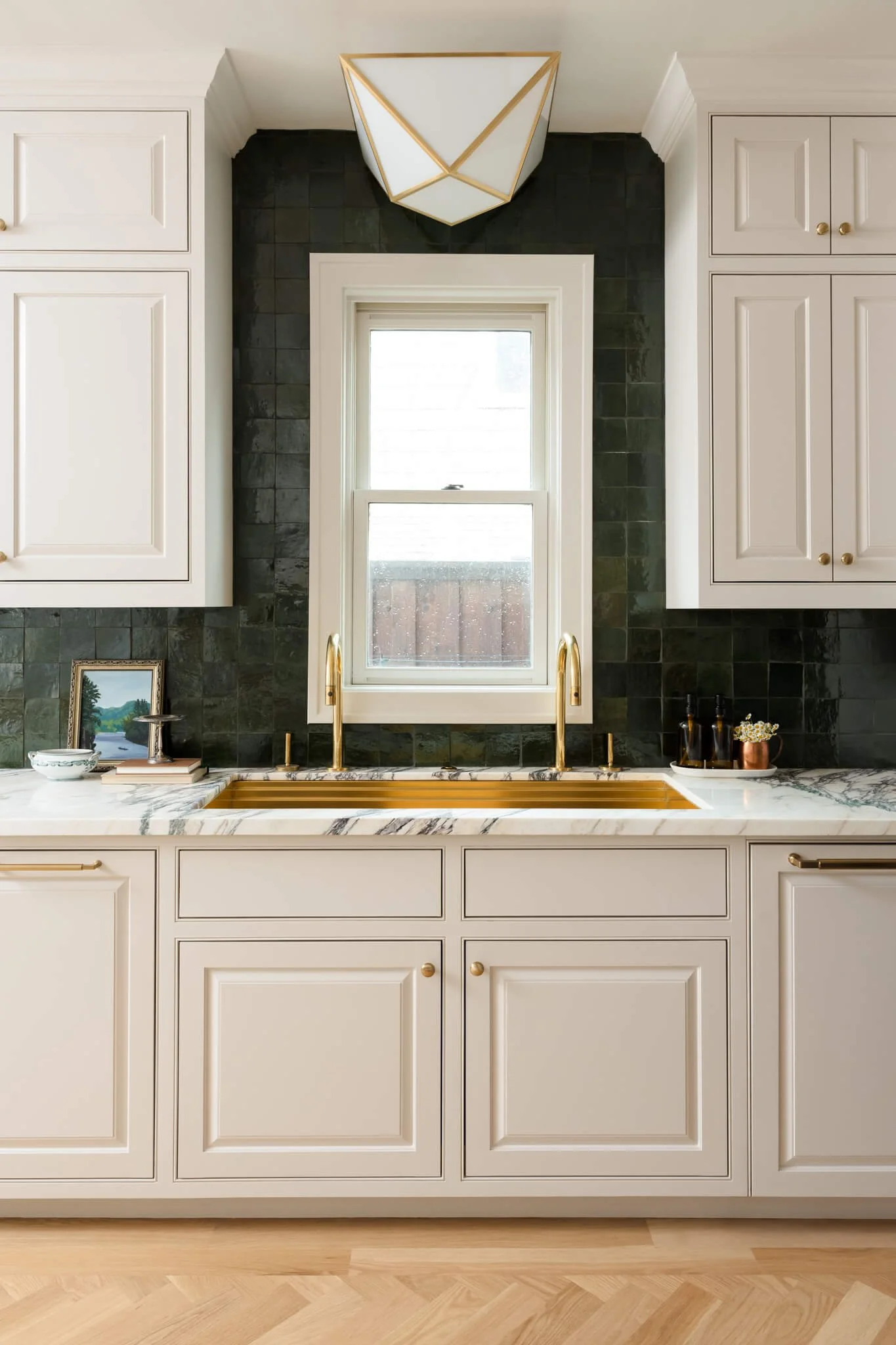 White kitchen with marble countertops, brass bridge faucet, and dark stone backsplash photographed for an interior design project.