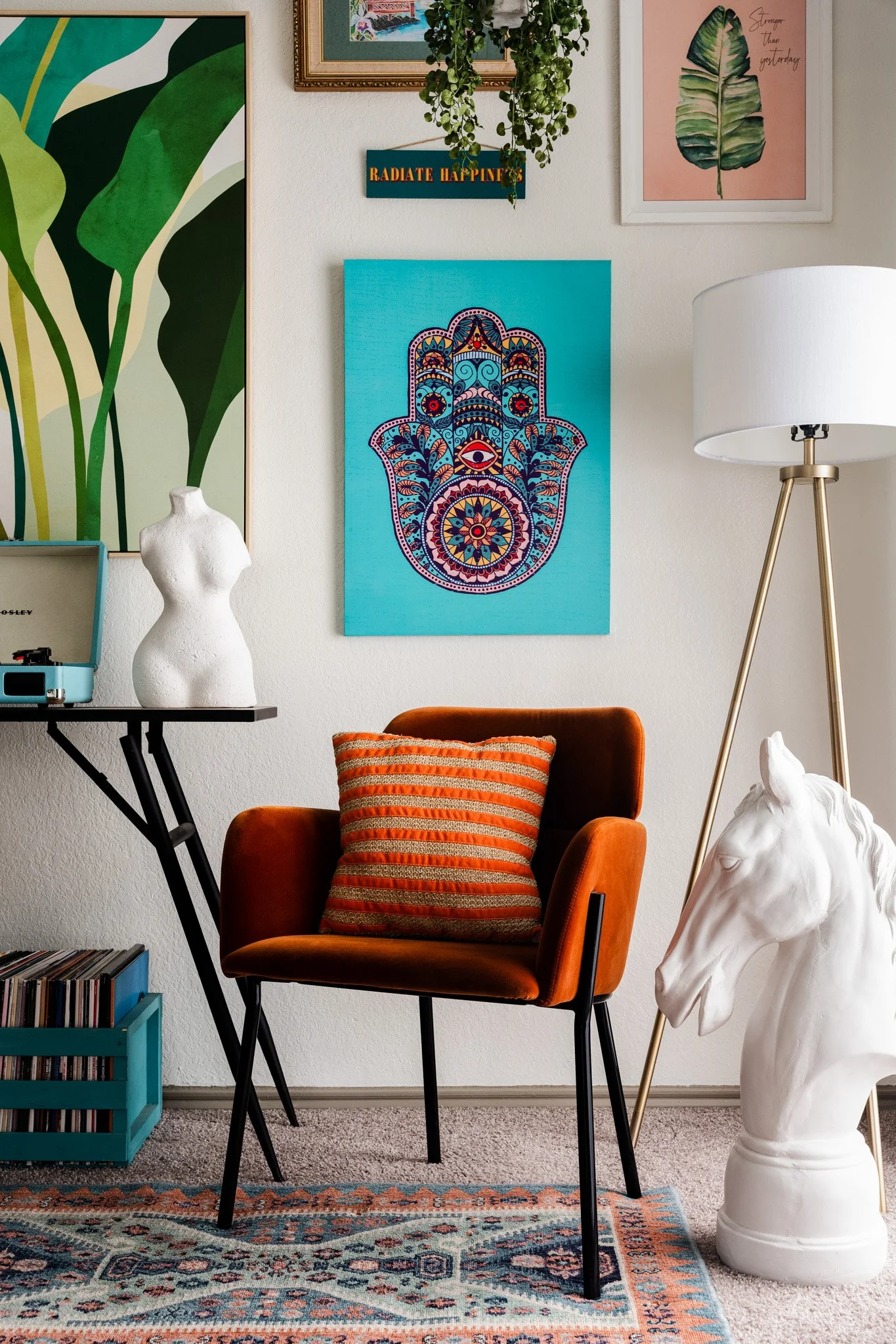 A cozy living room corner featuring a burnt orange upholstered armchair with a striped orange and gold pillow, a white ceramic horse head sculpture, a small turquoise vinyl record storage crate, and a colorful patterned rug