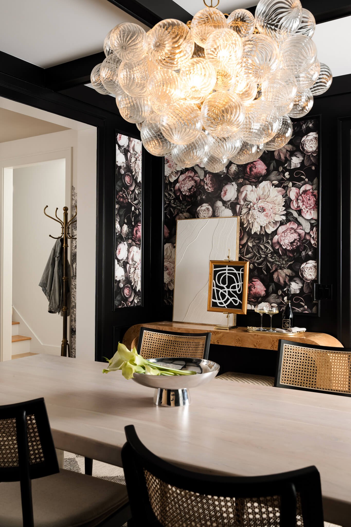 Editorial detail of floral wallpaper, woven console styling, and dramatic chandelier in a luxury dining room interior.