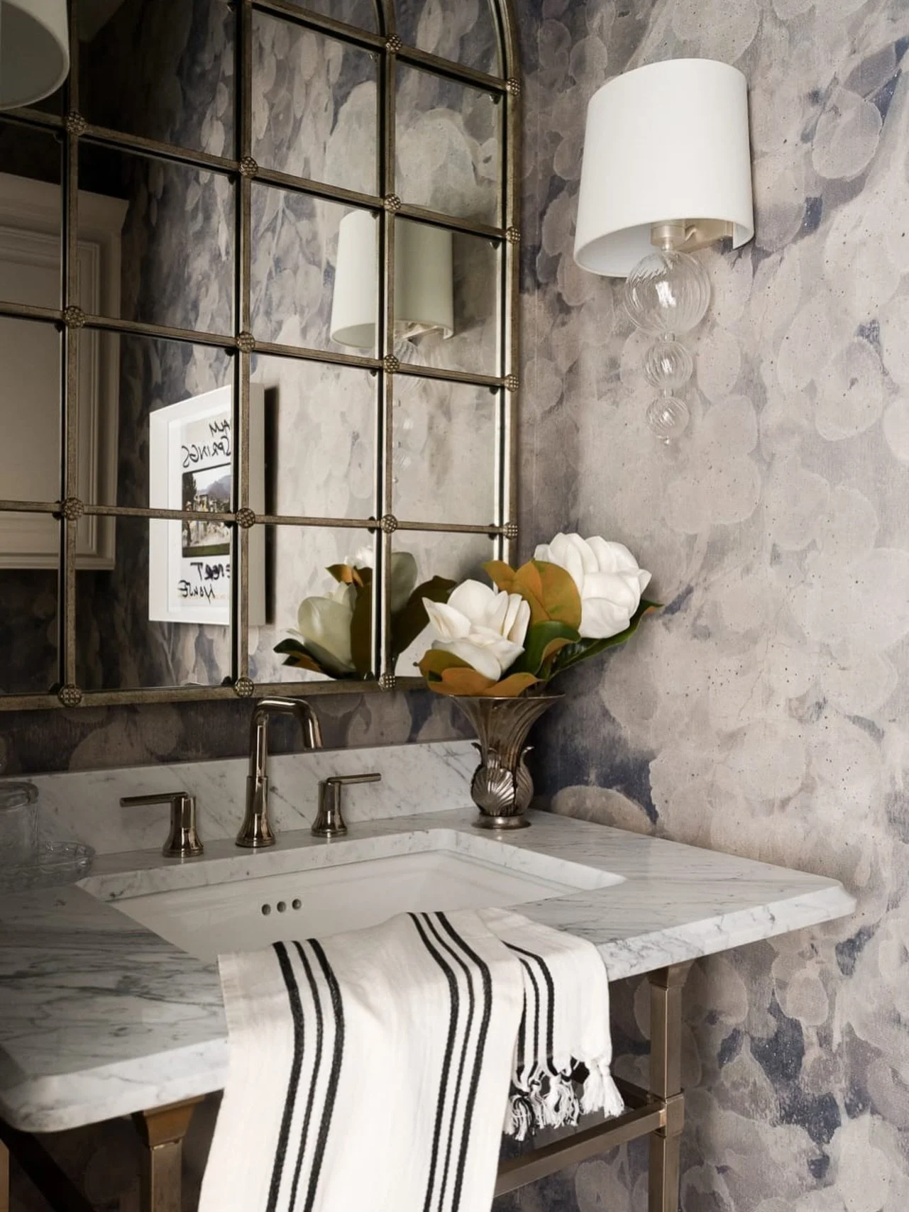 The most compelling rooms often come down to how different elements speak to one another.

Here, the movement of the marble is echoed by the painterly wallcovering, while the grid mirror introduces structure against all of that softness. Polished met