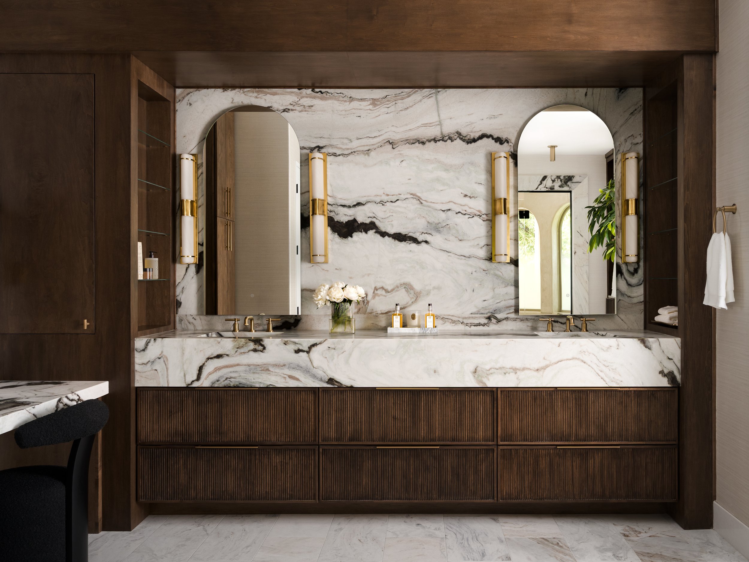 Bathroom vanity with marble countertop and wall, two mirrors, and wall-mounted light fixtures.