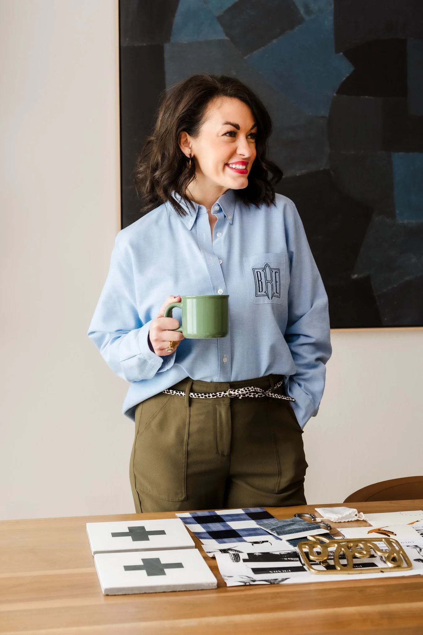 Interior designer Britney Ratto portrait holding coffee mug at styled workspace. 