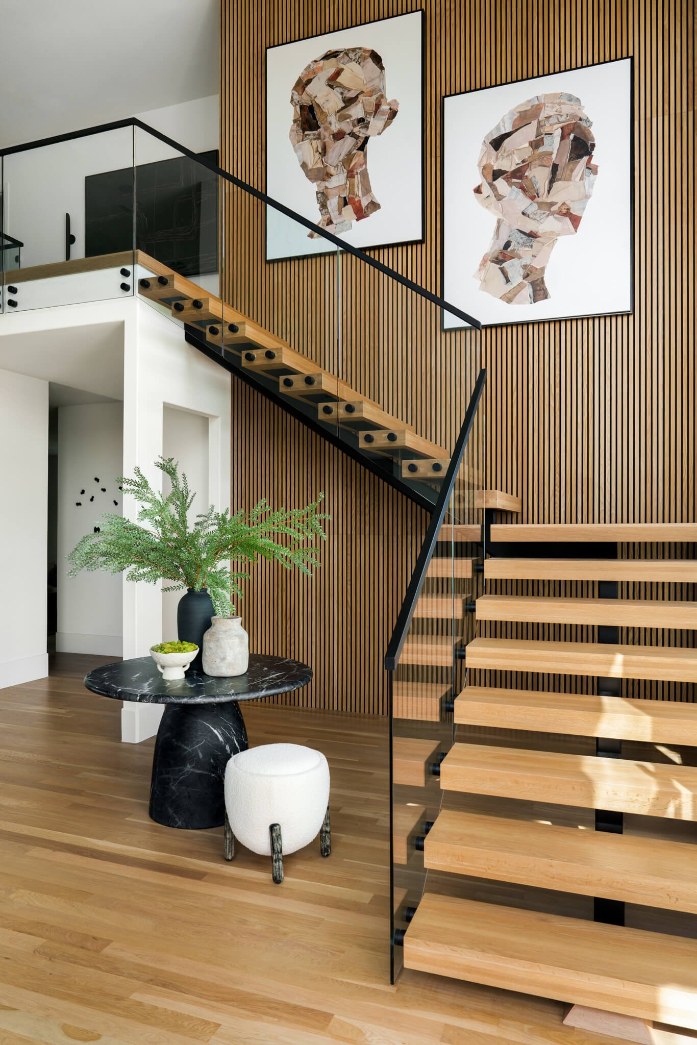 A modern interior with a staircase, wooden slat wall, and two large abstract portraits made of wood pieces hanging on the wall.