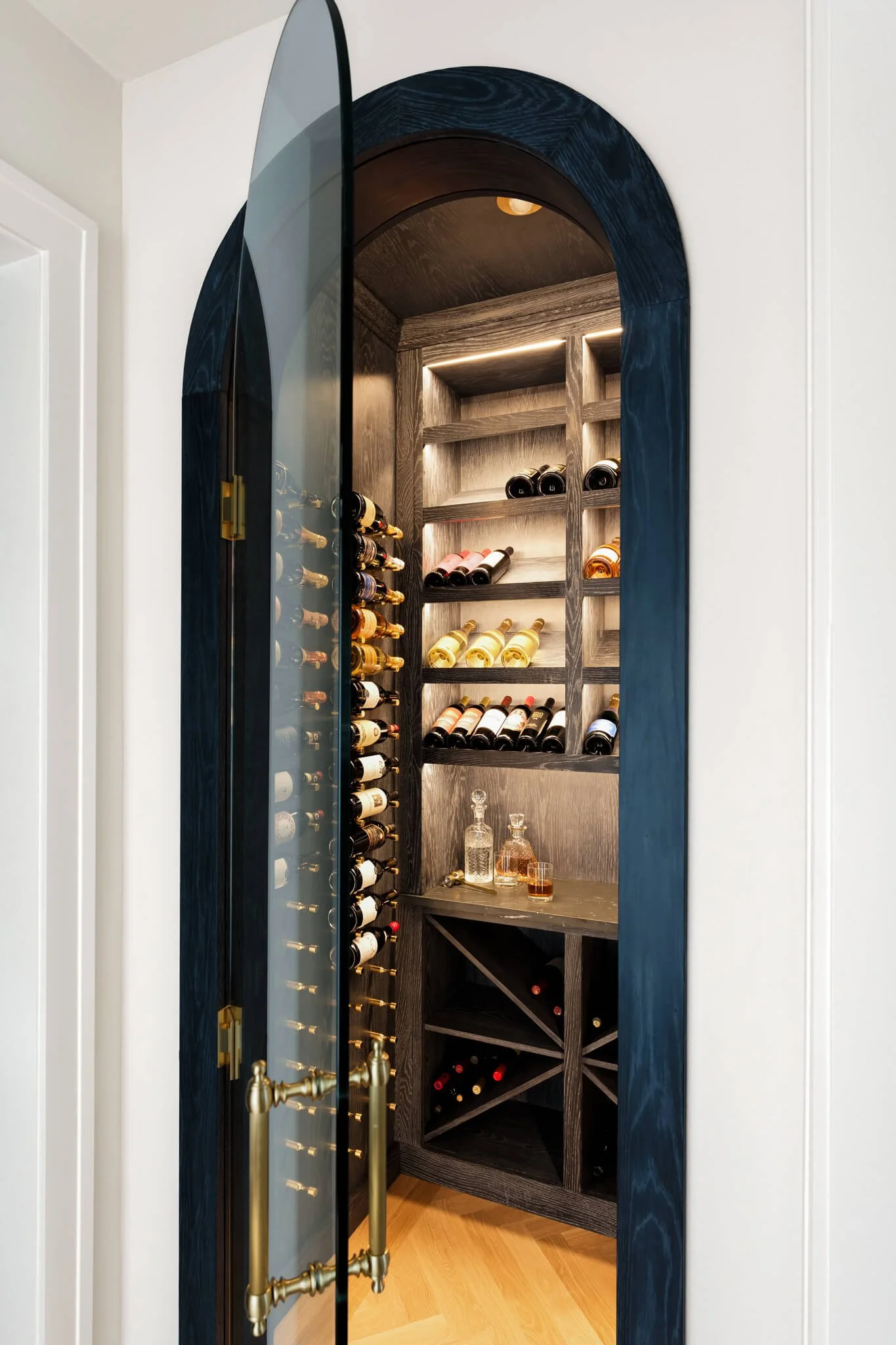 Custom wine cellar with arched blue entry doors, illuminated shelving, and luxury bottle storage design.