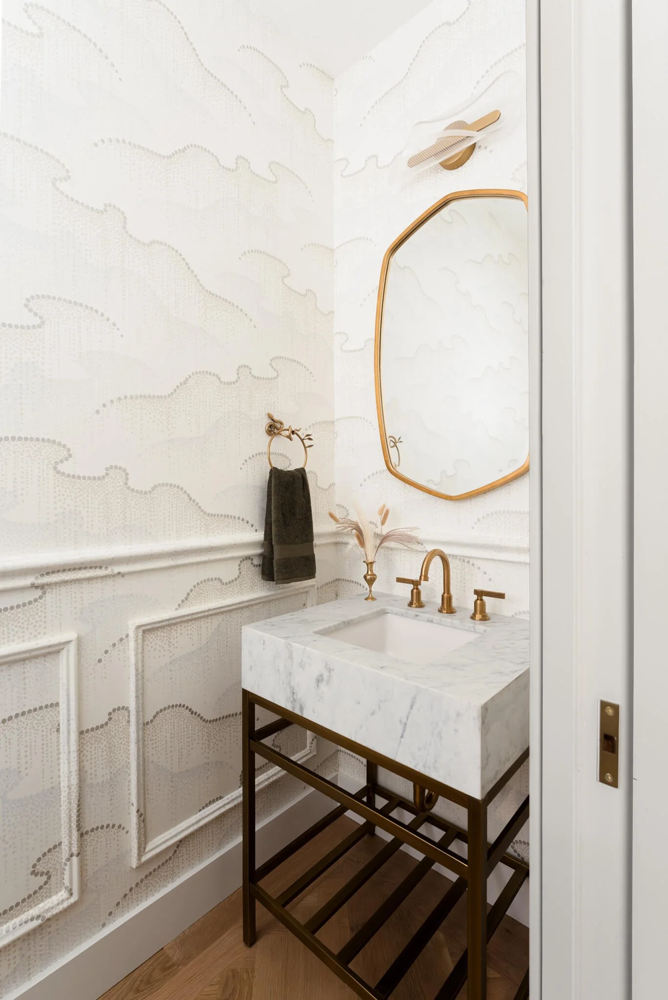 Luxury powder bathroom with marble vanity, textured plaster walls, and sculptural gold mirror in a modern Texas home.