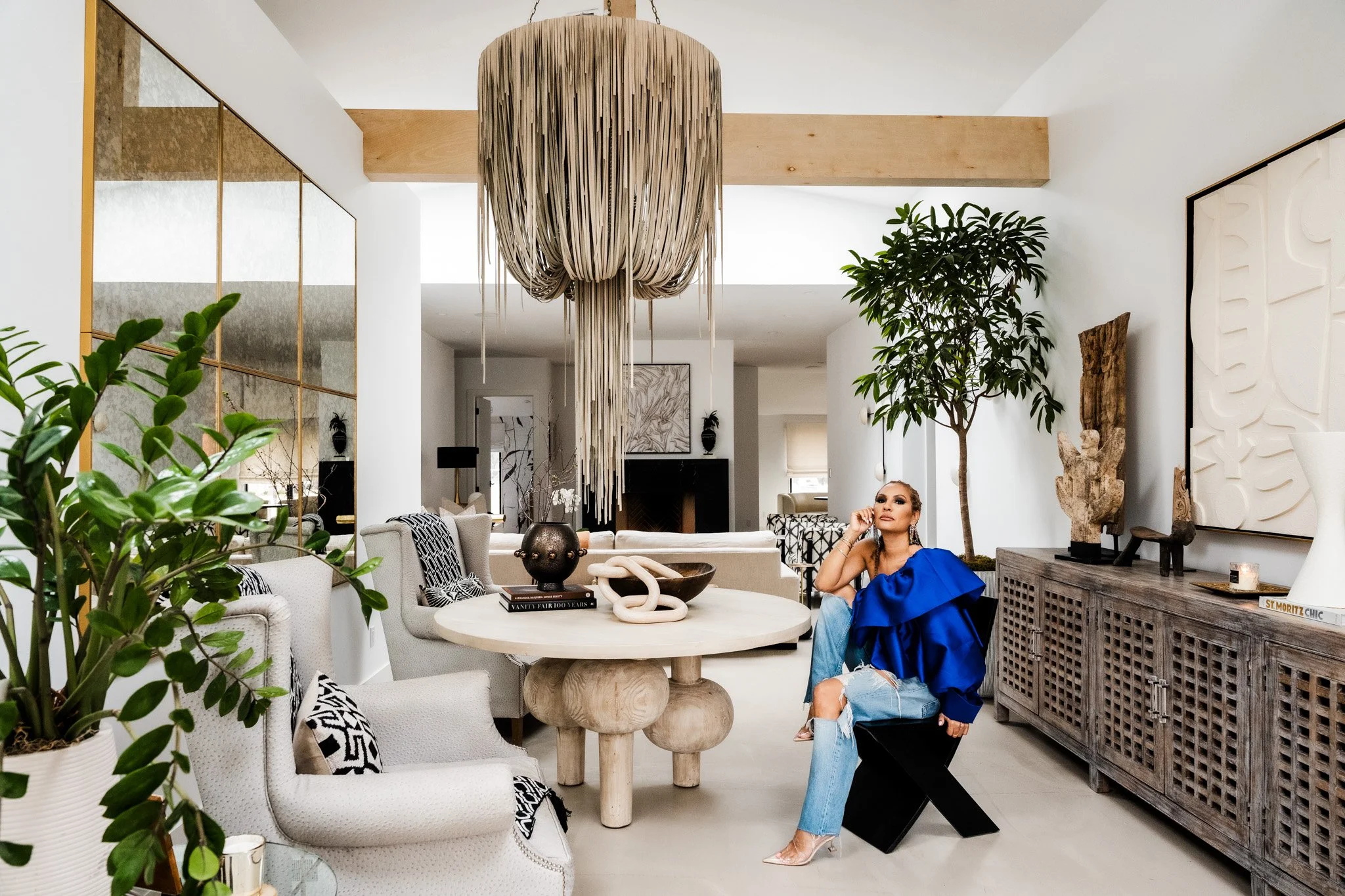 Bright sculptural living room with neutral palette and designer seated in blue outfit. Nikki Chu Home 