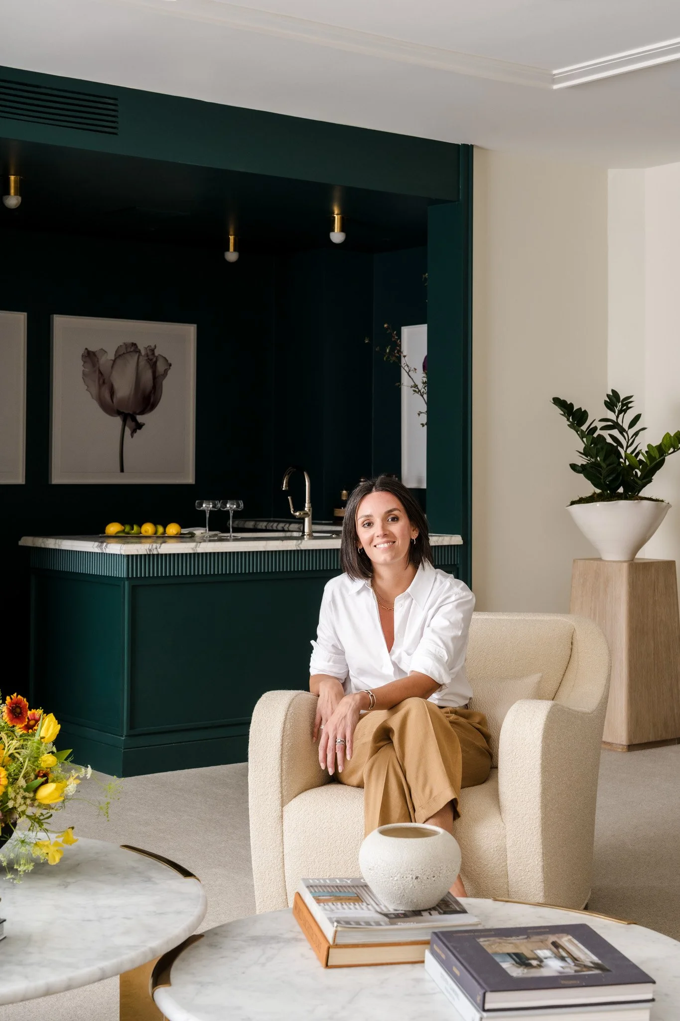 Interior designer seated in green kitchen with marble island and soft styling. 