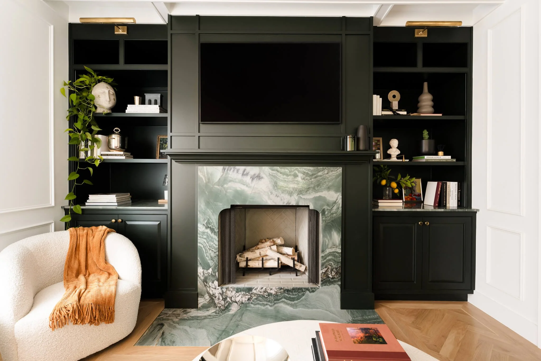 Moody living room with black built-in shelving, marble fireplace surround, and warm layered styling details.