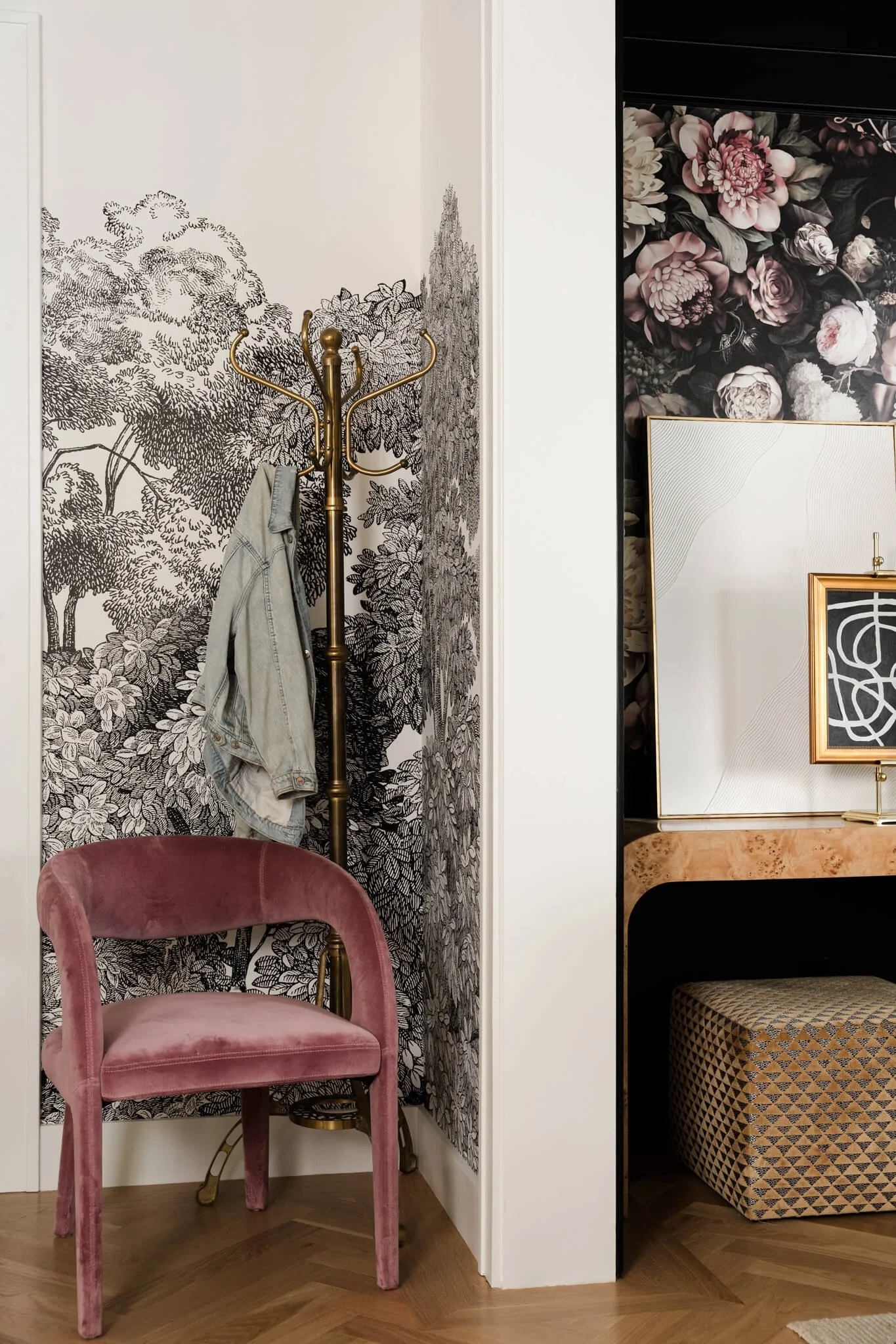 Moody entryway detail featuring floral wallpaper, blush velvet chair, and brass coat hooks in a luxury residential interior.