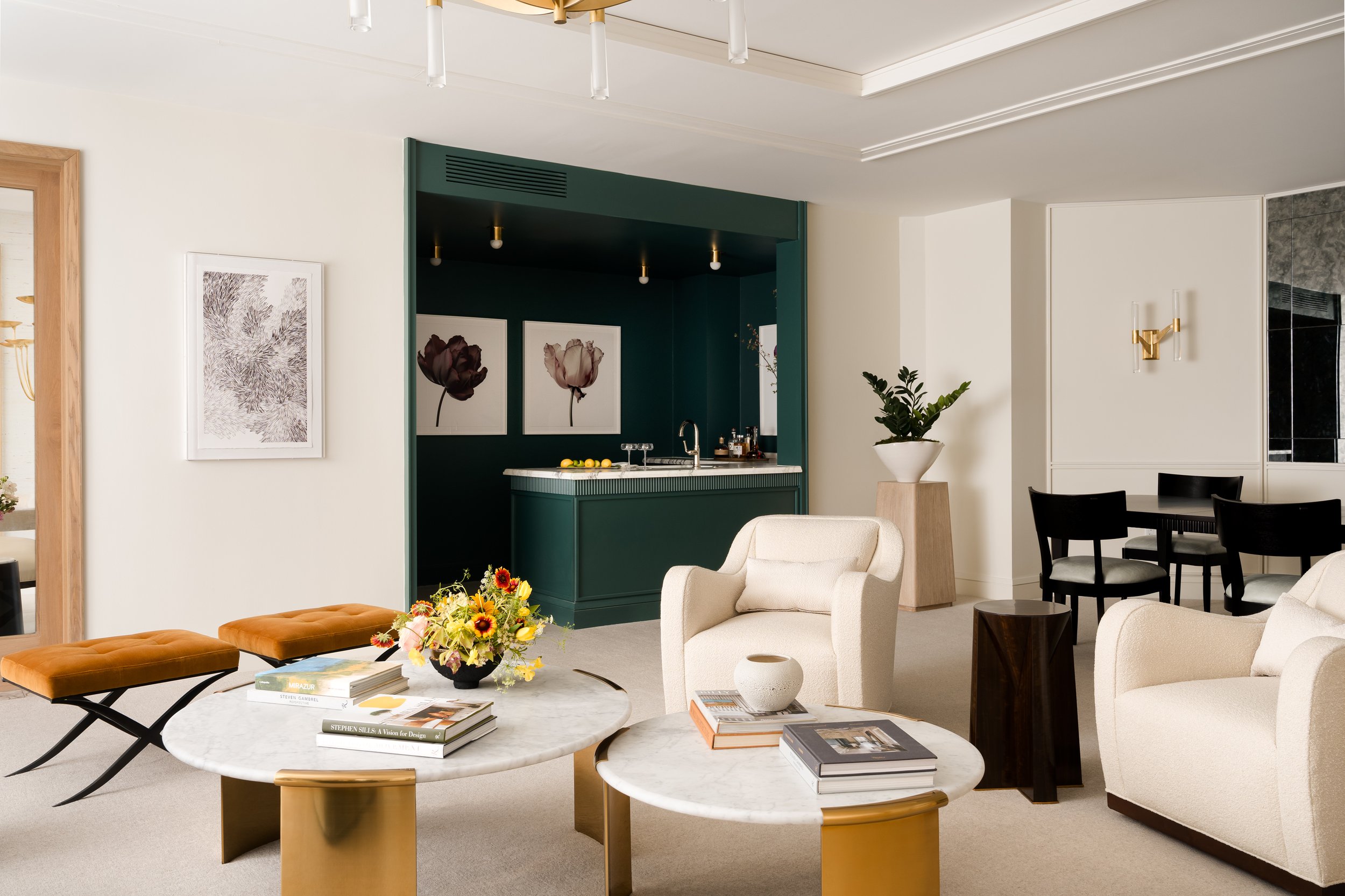 Living room with beige furniture, marble coffee tables, a green kitchenette, and artwork of flowers on the walls.