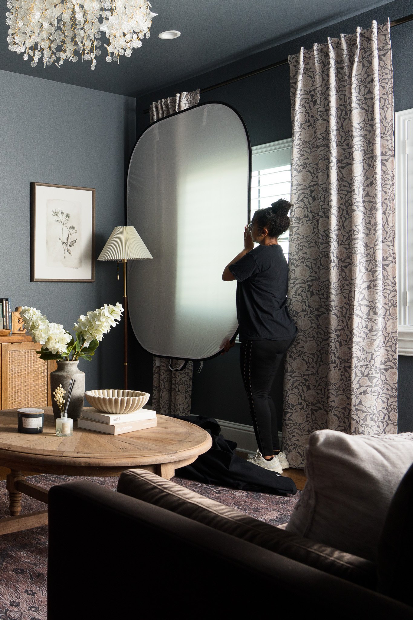 a photographer assistant holding up a white reflector to block the window reflection in the wall art at an interior design photography session.