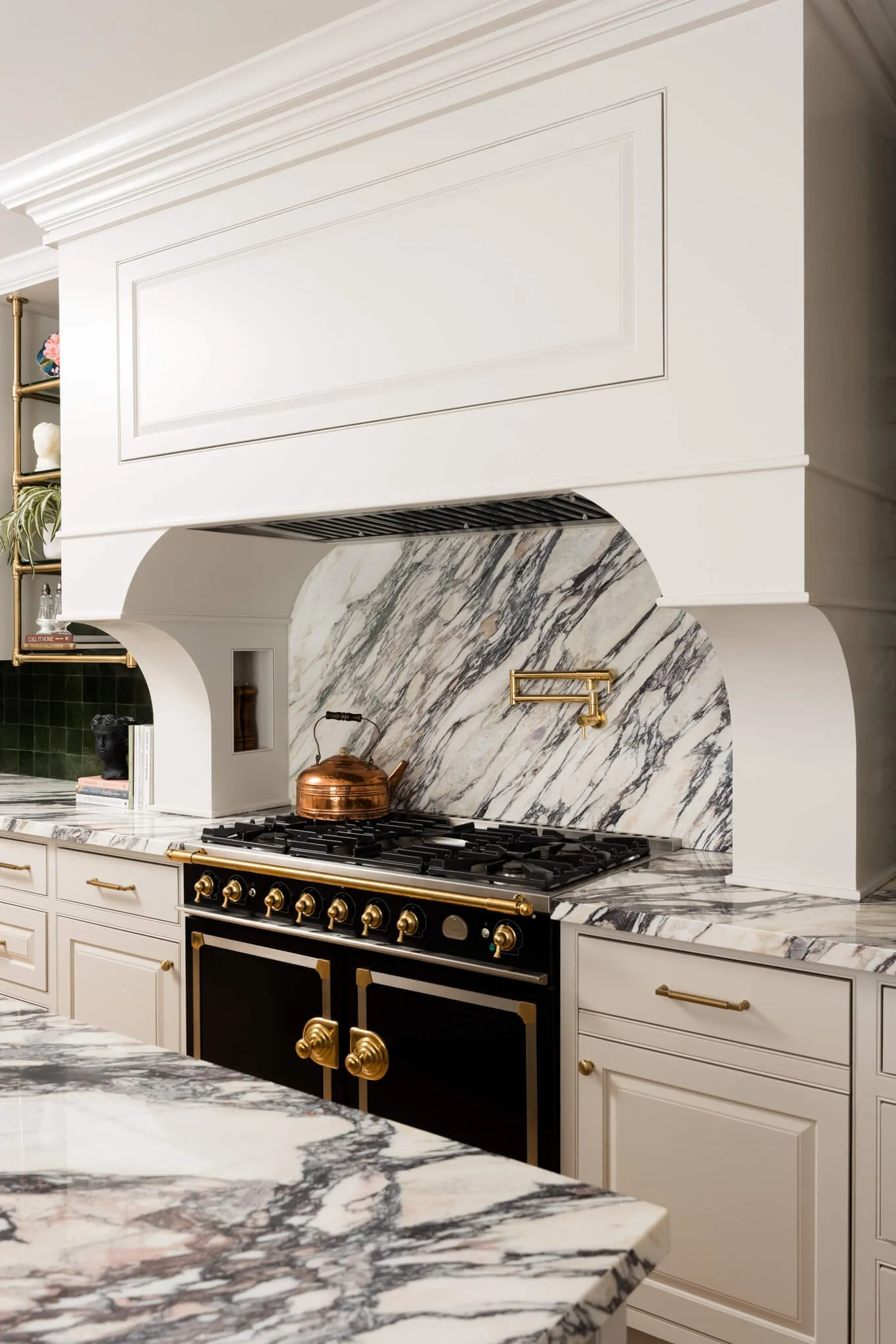 Luxury marble kitchen range with custom plaster hood, brass pot filler, and dramatic stone backsplash.