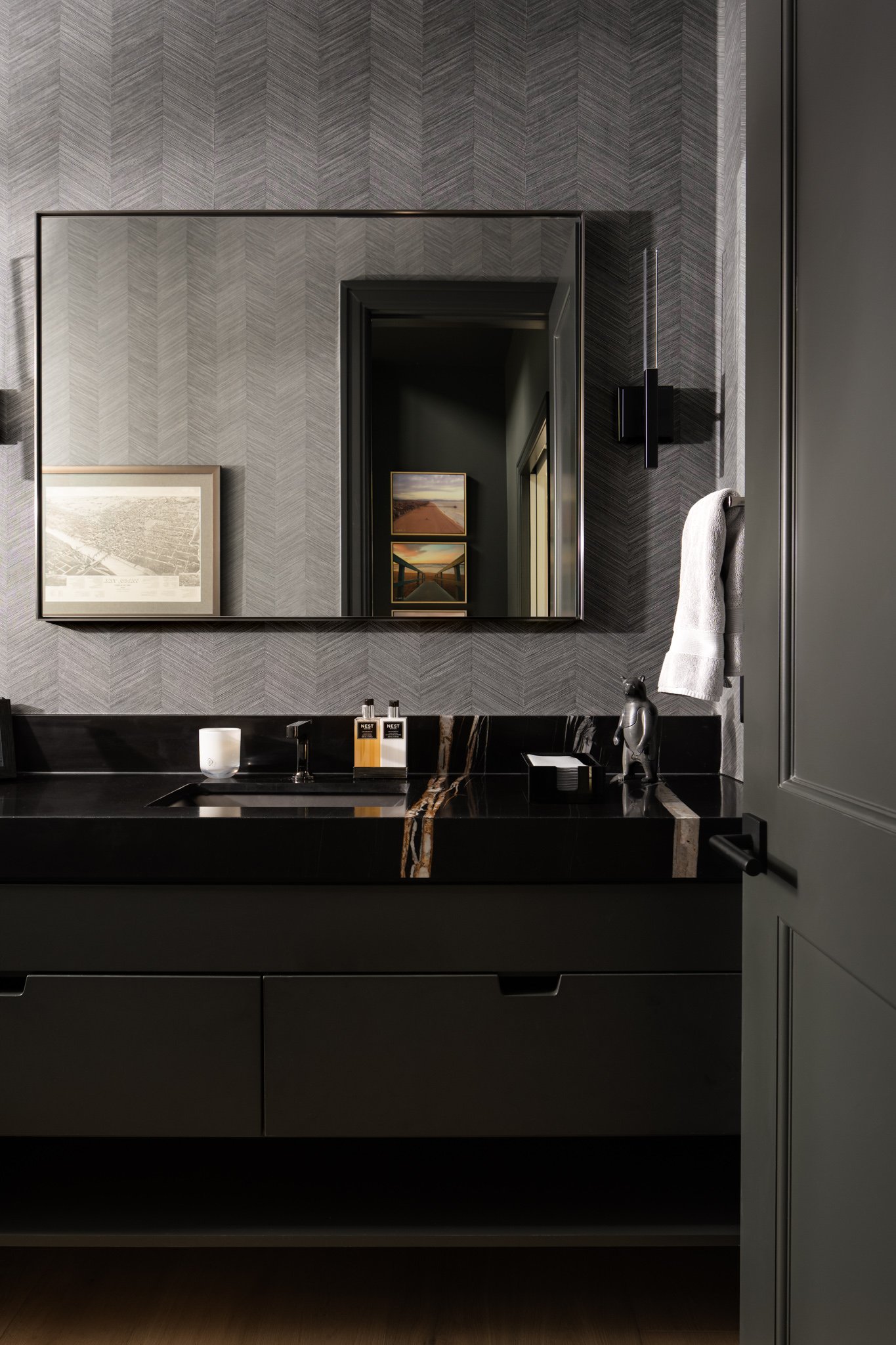 Bathroom with dark vanity, marble countertop, wall-mounted mirror, wall-mounted light fixture, and hand towel hanging on a hook.