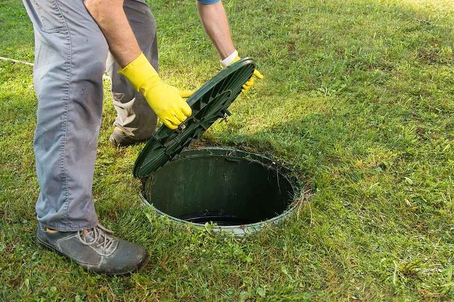 A worker opens the access lid of a newly installed septic tank during a septic system installation on residential property.