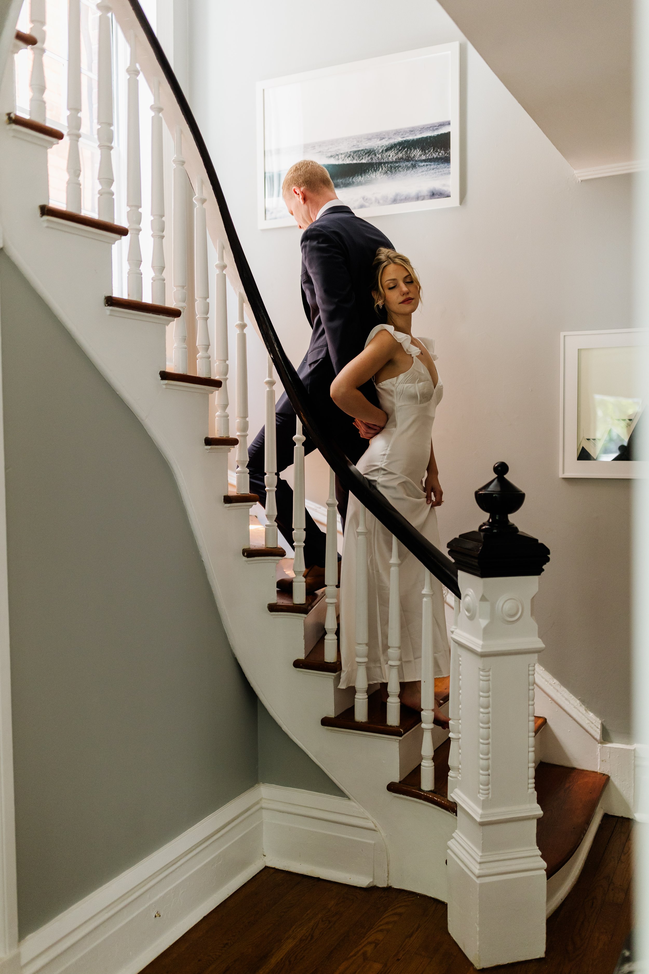 First touch with bride in a white dress and groom in a black suit standing on a staircase, with the woman leaning her back against a man's chest.