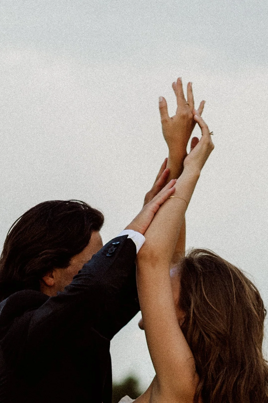 Two women and a man with their hands raised and intertwined, set against a clear sky, symbolizing unity or celebration.